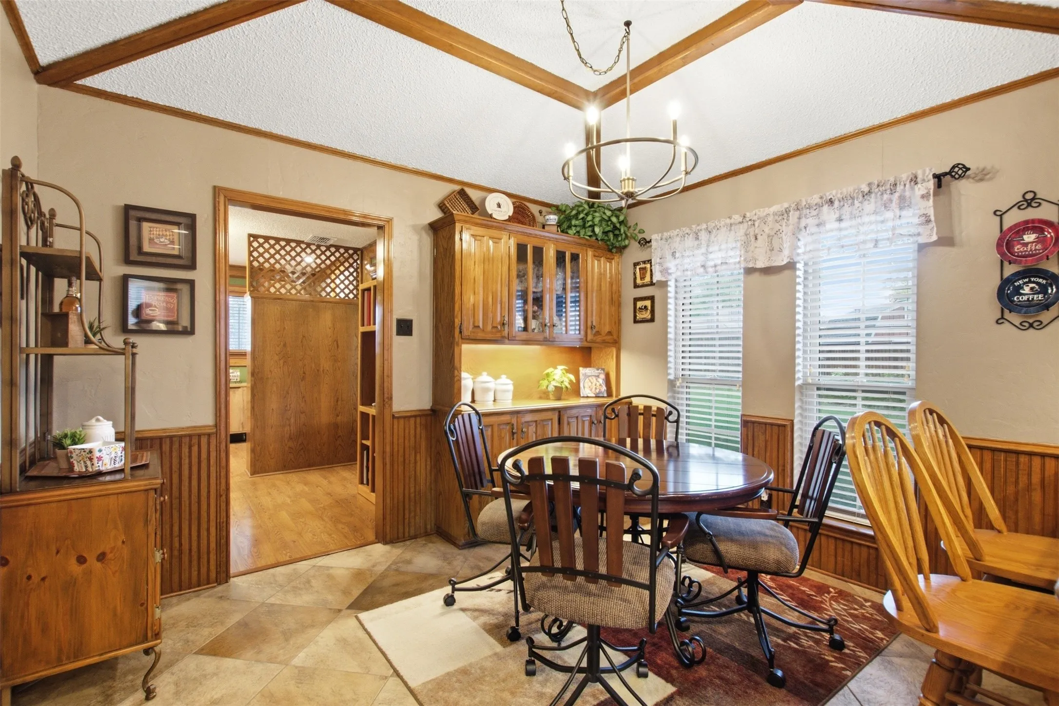 Dining area featuring a decorative ceiling with wood beams, a built-in buffet with glass-front cabinetry, two large windows with blinds, and geometric tile flooring