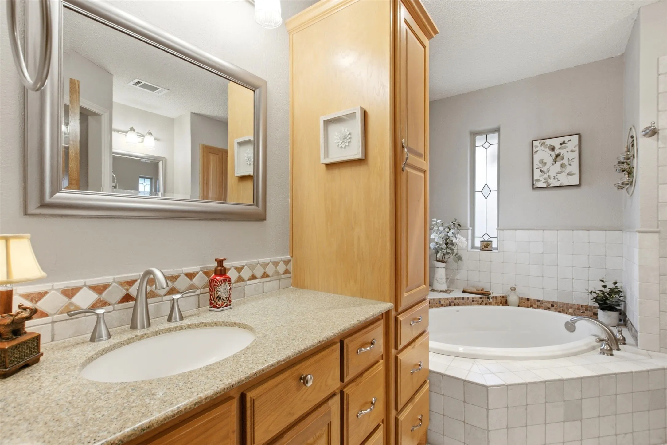 Bathroom featuring a garden tub with tile surround, a built-in vanity with a granite countertop, an undermount sink with brushed nickel fixtures, and a tall built-in linen cabinet
