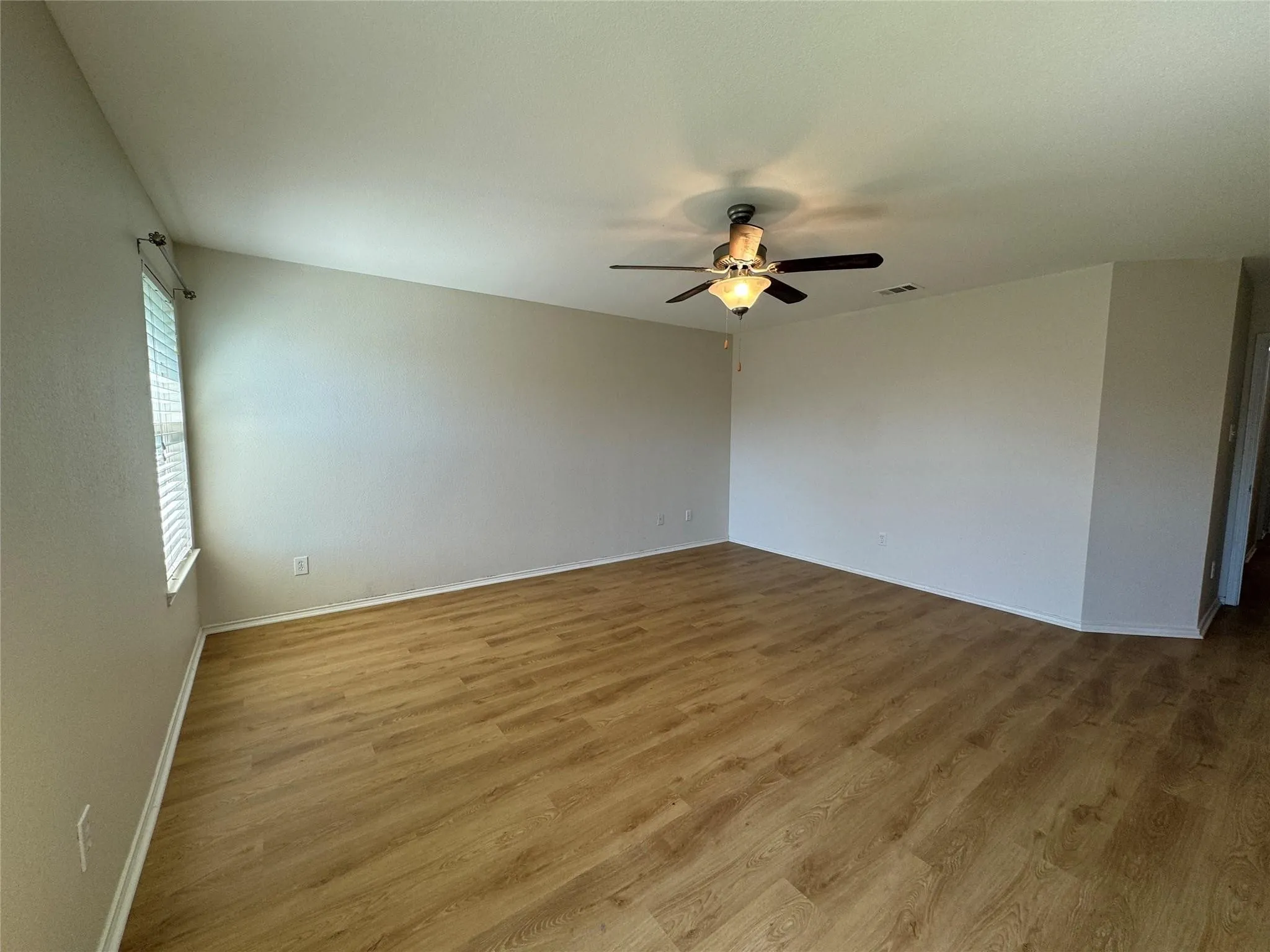 Spacious room featuring wood-finish flooring, a contemporary ceiling fan with integrated lighting, and a single window with blinds
