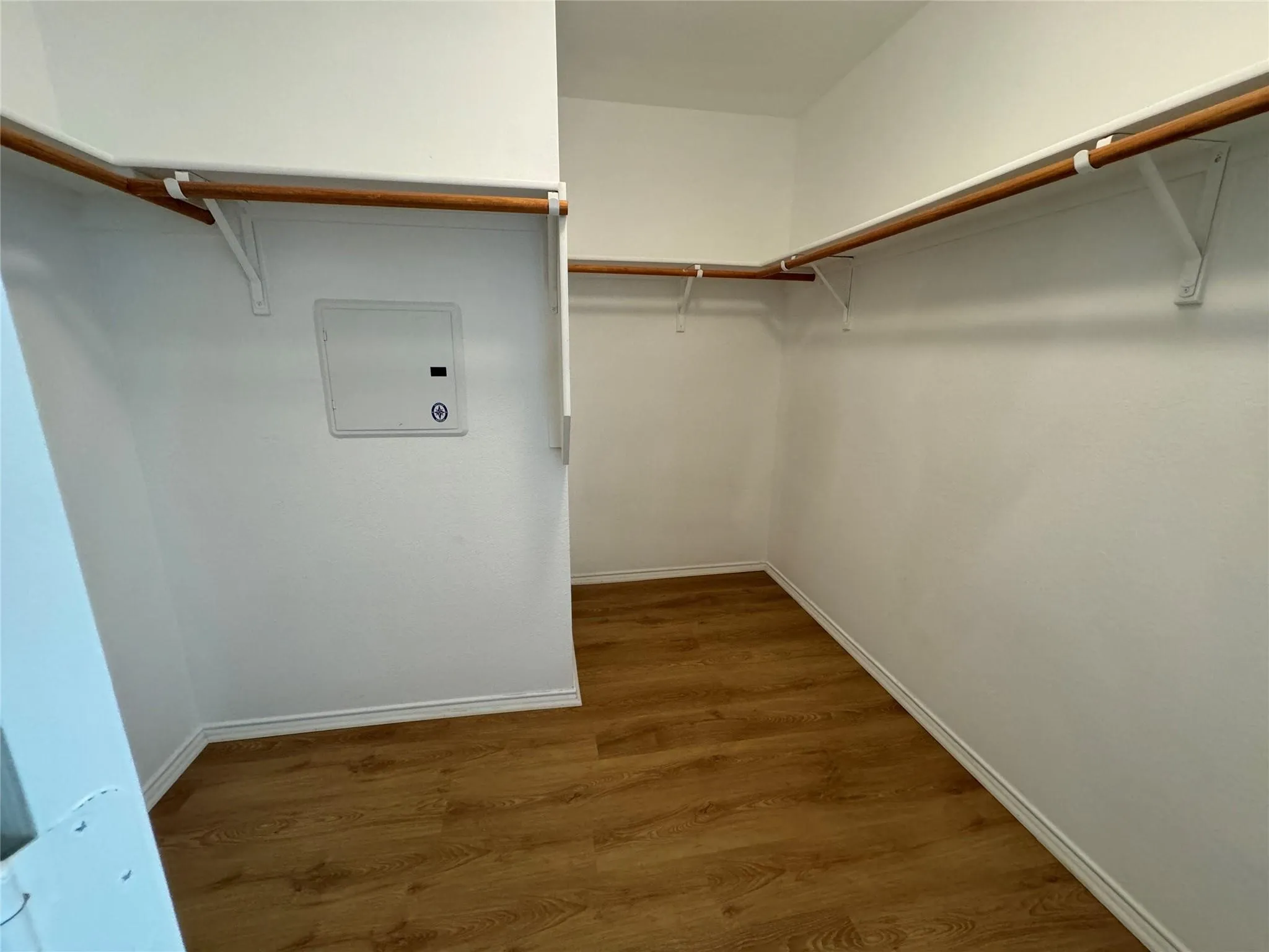 Spacious walk-in closet featuring wood-finish flooring, white walls, white baseboards, and two levels of clothes rods