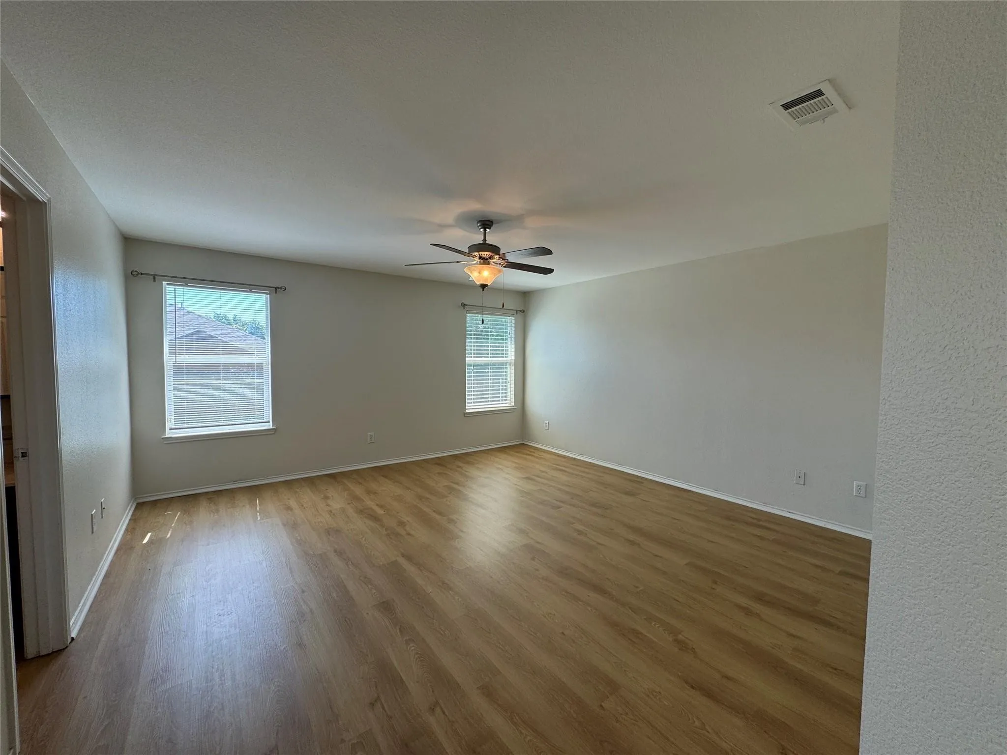 Spacious interior room featuring wood-finish flooring, light-toned walls, and a ceiling fan with integrated lighting