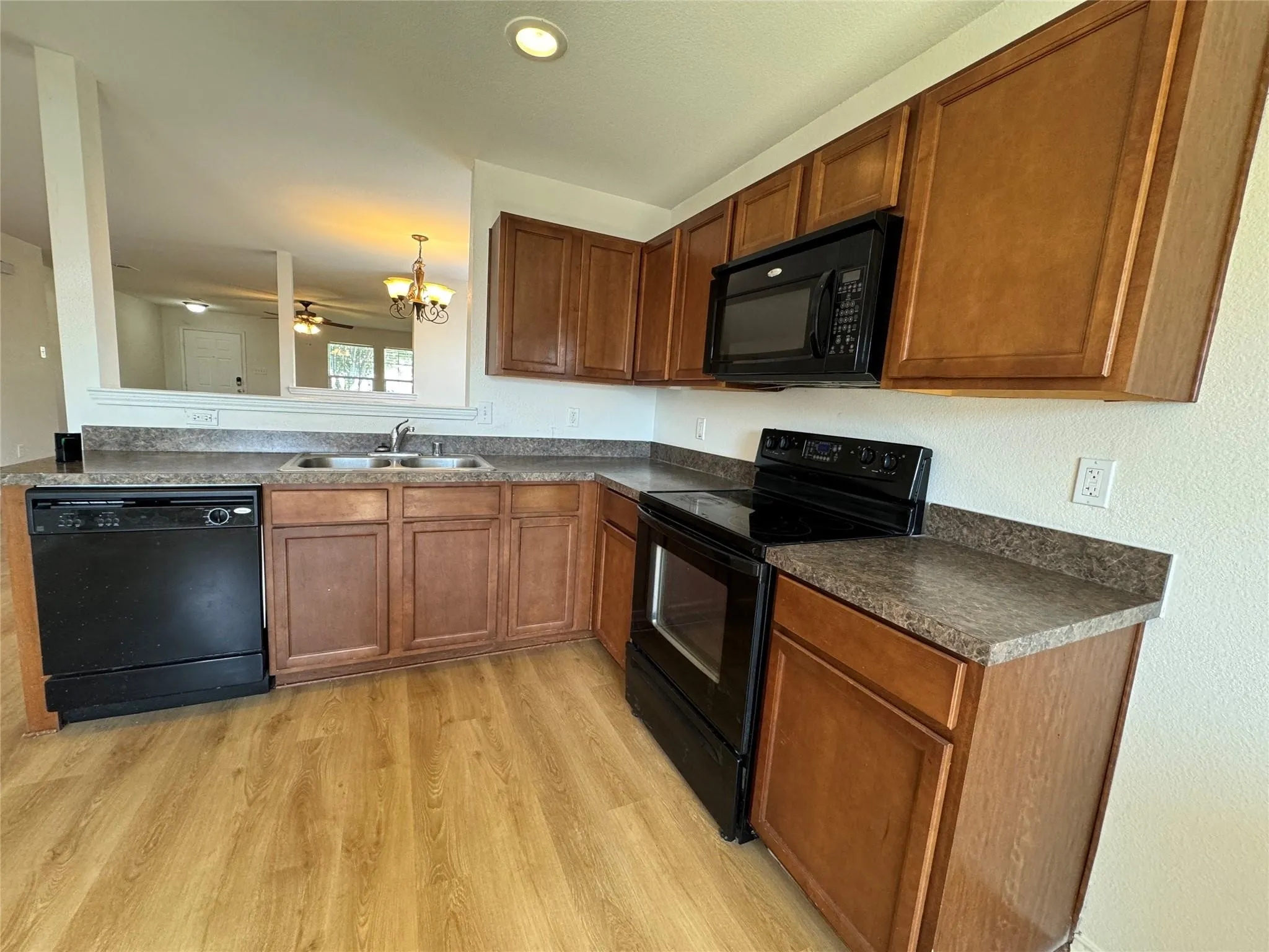 Kitchen featuring wood-finish flooring, dark speckled countertops, wood cabinetry, a black built-in microwave, and a black electric range