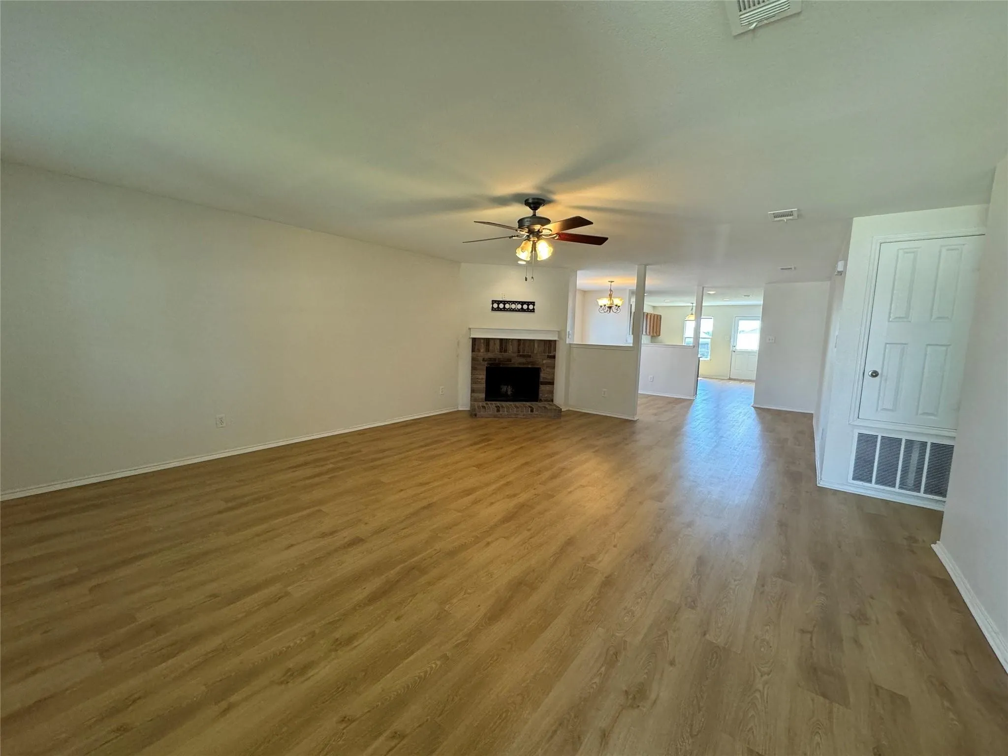 Spacious living area featuring wood-finish flooring, a brick fireplace with a white mantel, and a ceiling fan with integrated lighting
