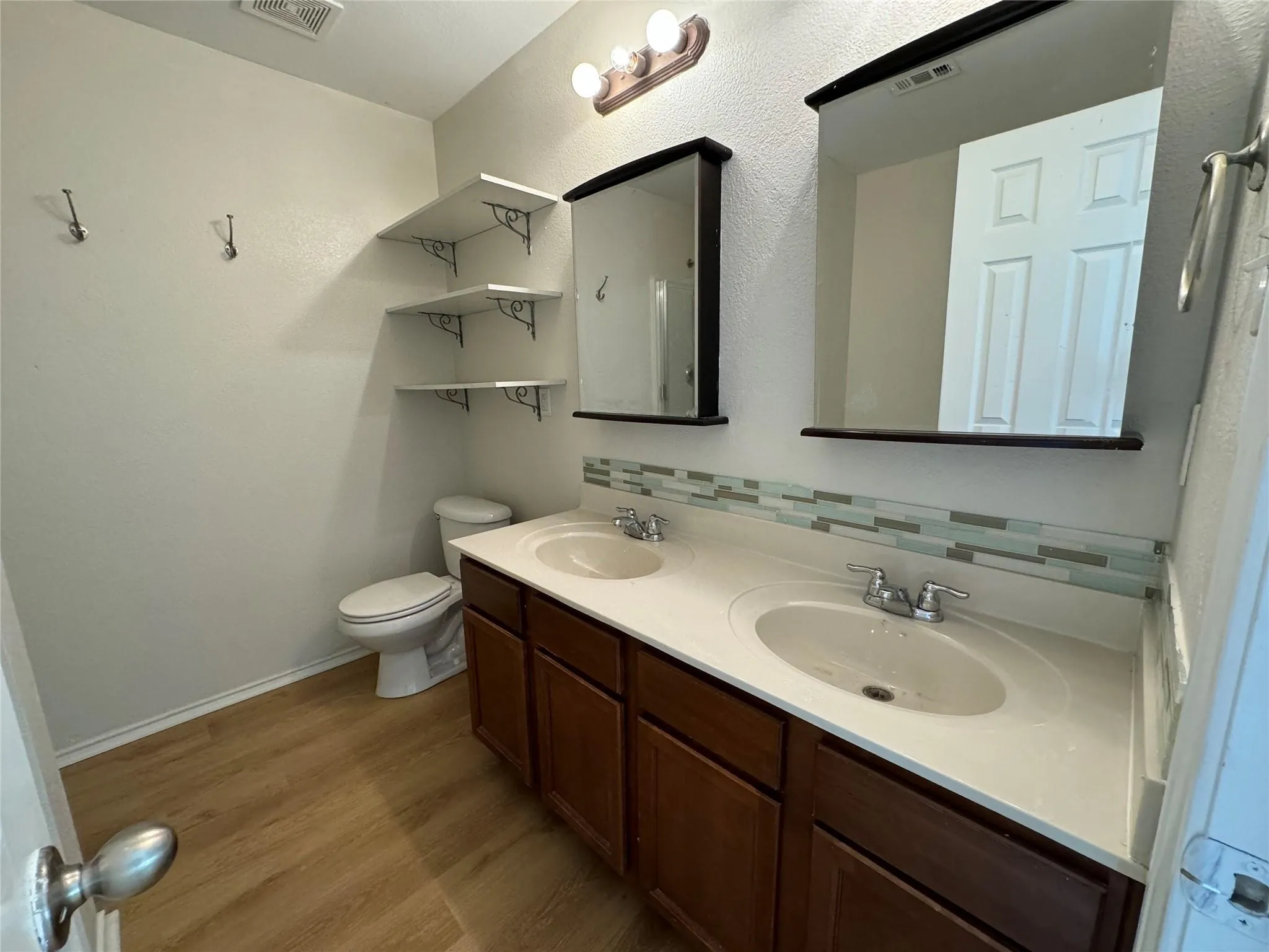 Dual vanity with integrated white sinks, wood-finish cabinetry, and a multi-tone tile backsplash