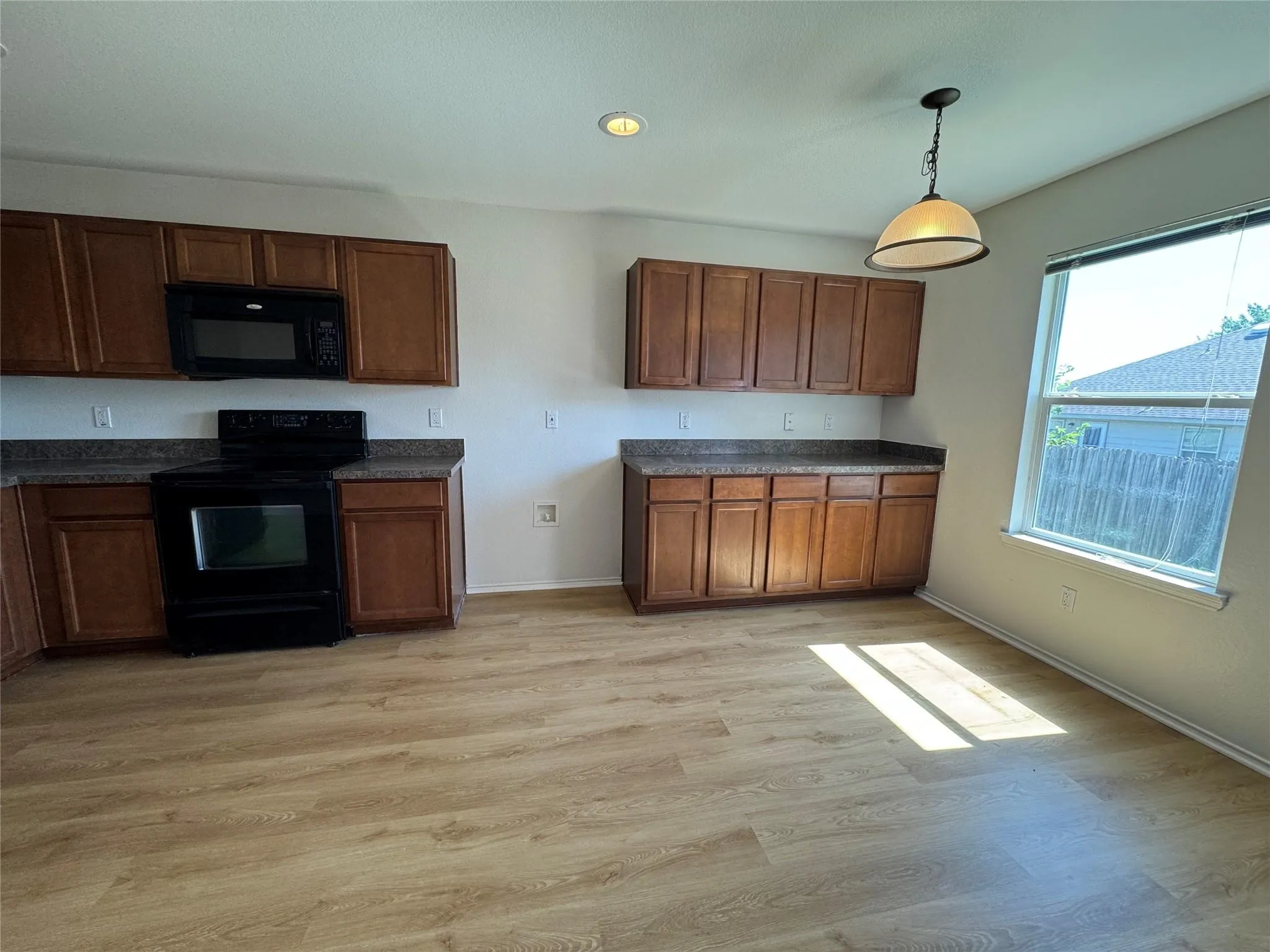 Kitchen featuring wood-finish flooring, dark wood cabinetry, black appliances, and a window with blinds
