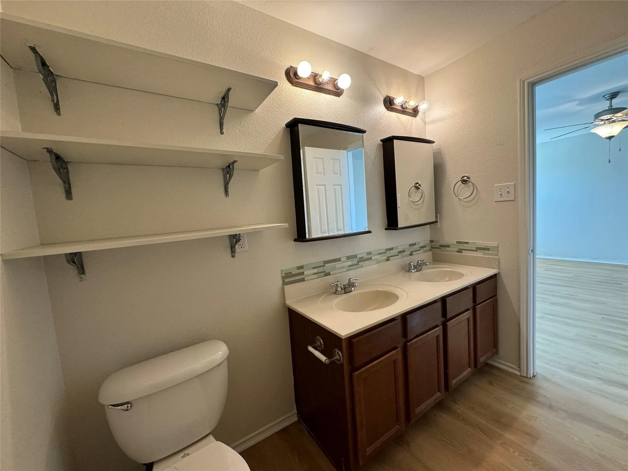 Bathroom vanity featuring dual sinks, a mosaic tile backsplash, and two framed medicine cabinets with integrated lighting