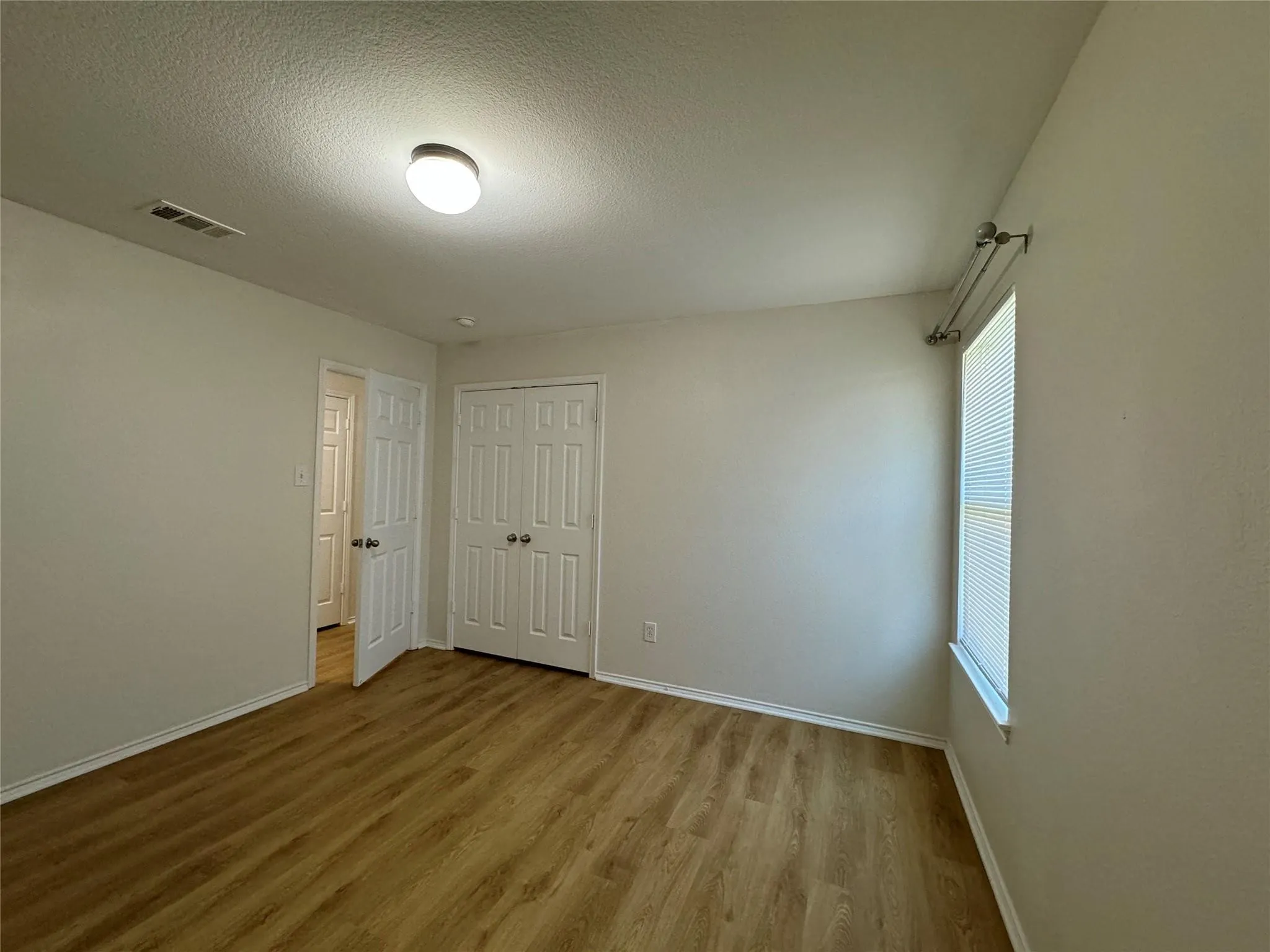 Light-filled room featuring wood-finish flooring, white baseboards, and a window with blinds