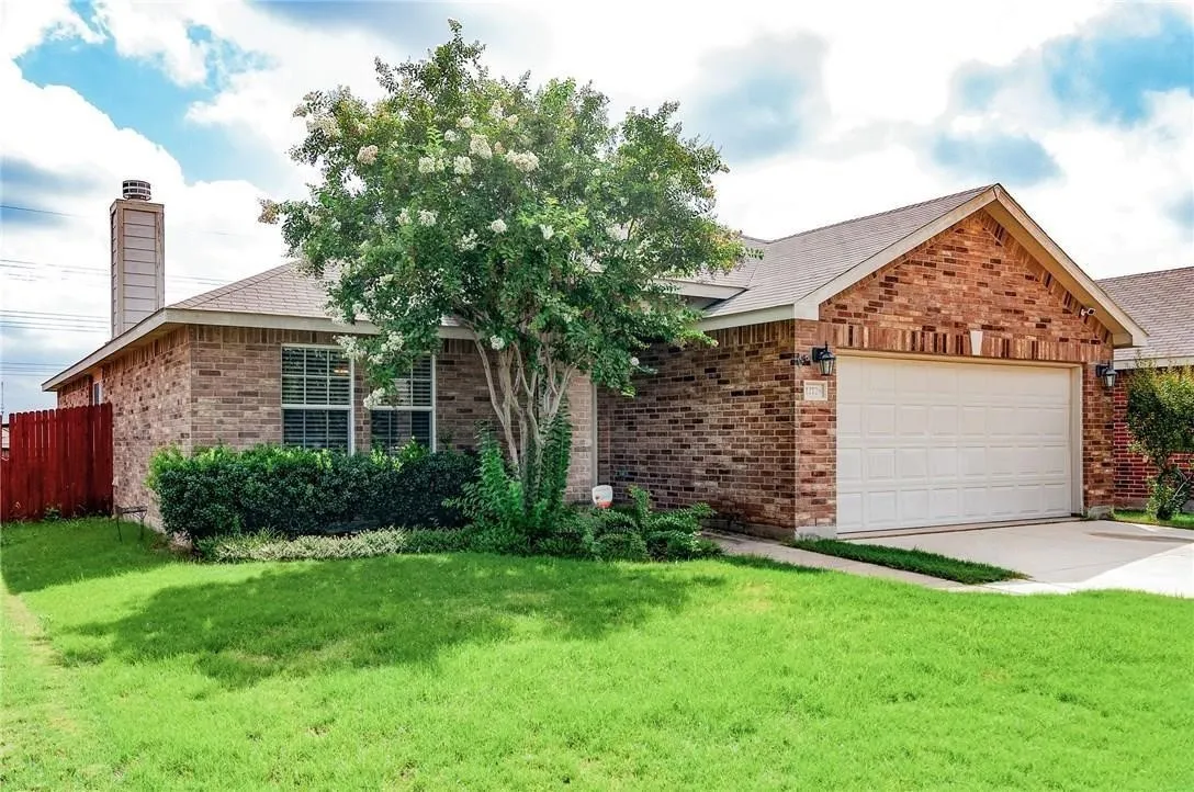 Brick exterior featuring a two-car garage, mature landscaping, and a red privacy fence