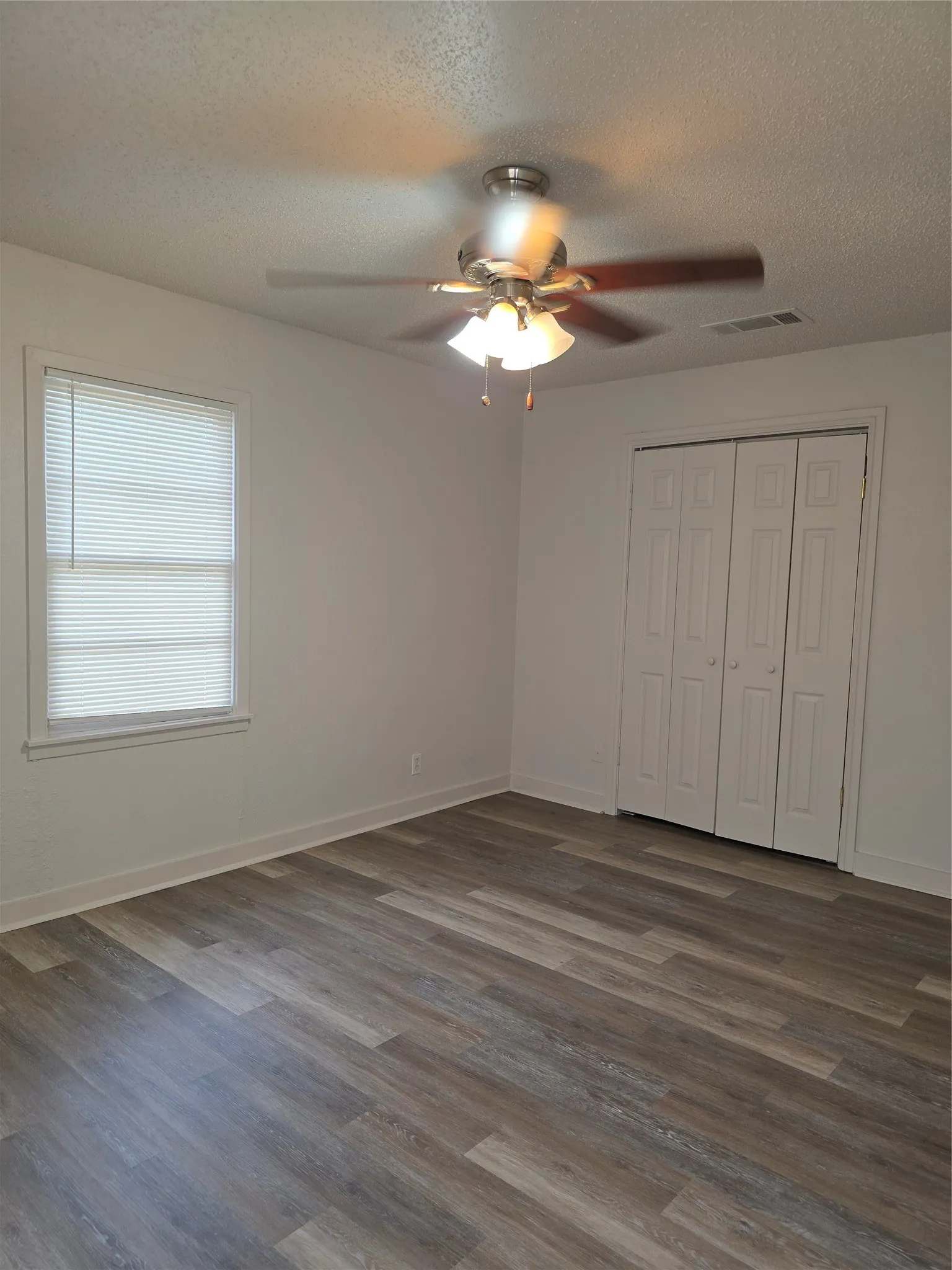 Spacious room featuring wood-finish flooring, white walls, and a ceiling fan with integrated lighting