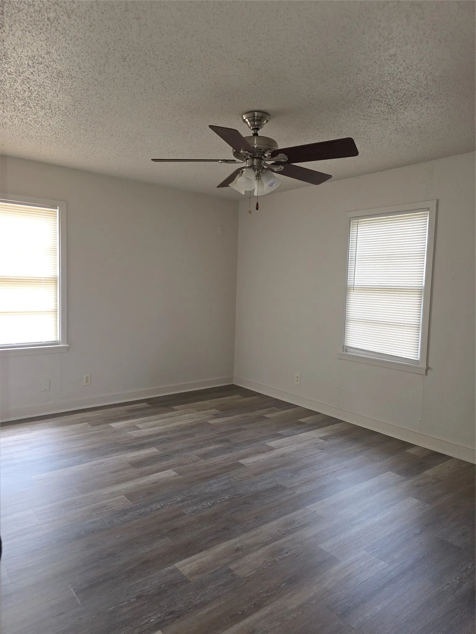 Spacious room featuring wood-finish flooring, light neutral wall tones, and a ceiling fan with integrated lighting