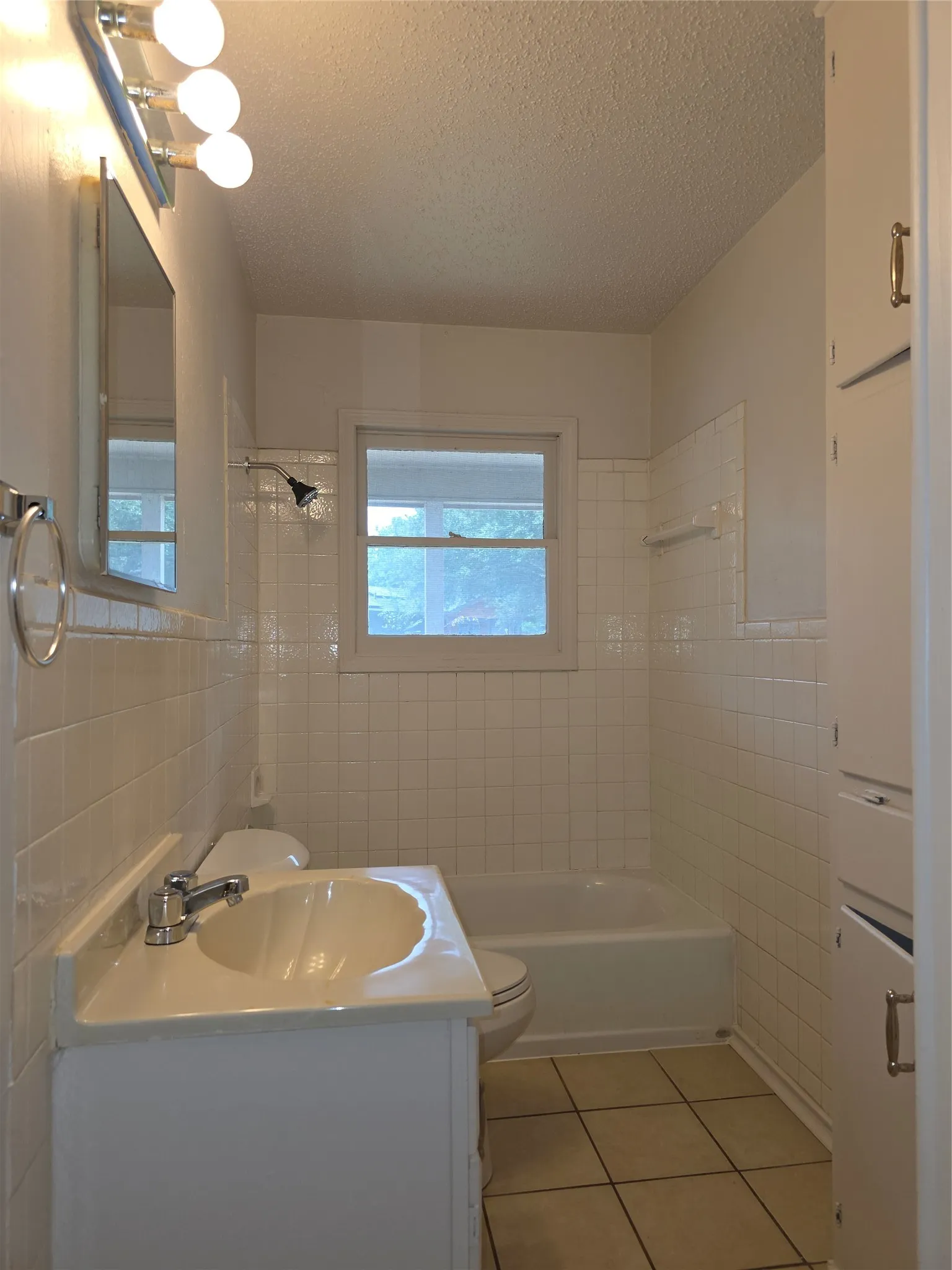 Bathroom featuring a white vanity with integrated sink, white subway tile surround, white tub, window, and tile flooring