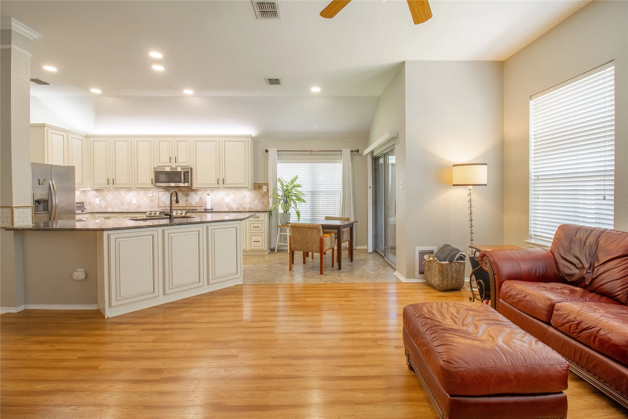 Open-concept living area featuring wood-finish flooring, a kitchen with off-white cabinetry, dark countertops, and stainless steel appliances, and a dining area with tile flooring