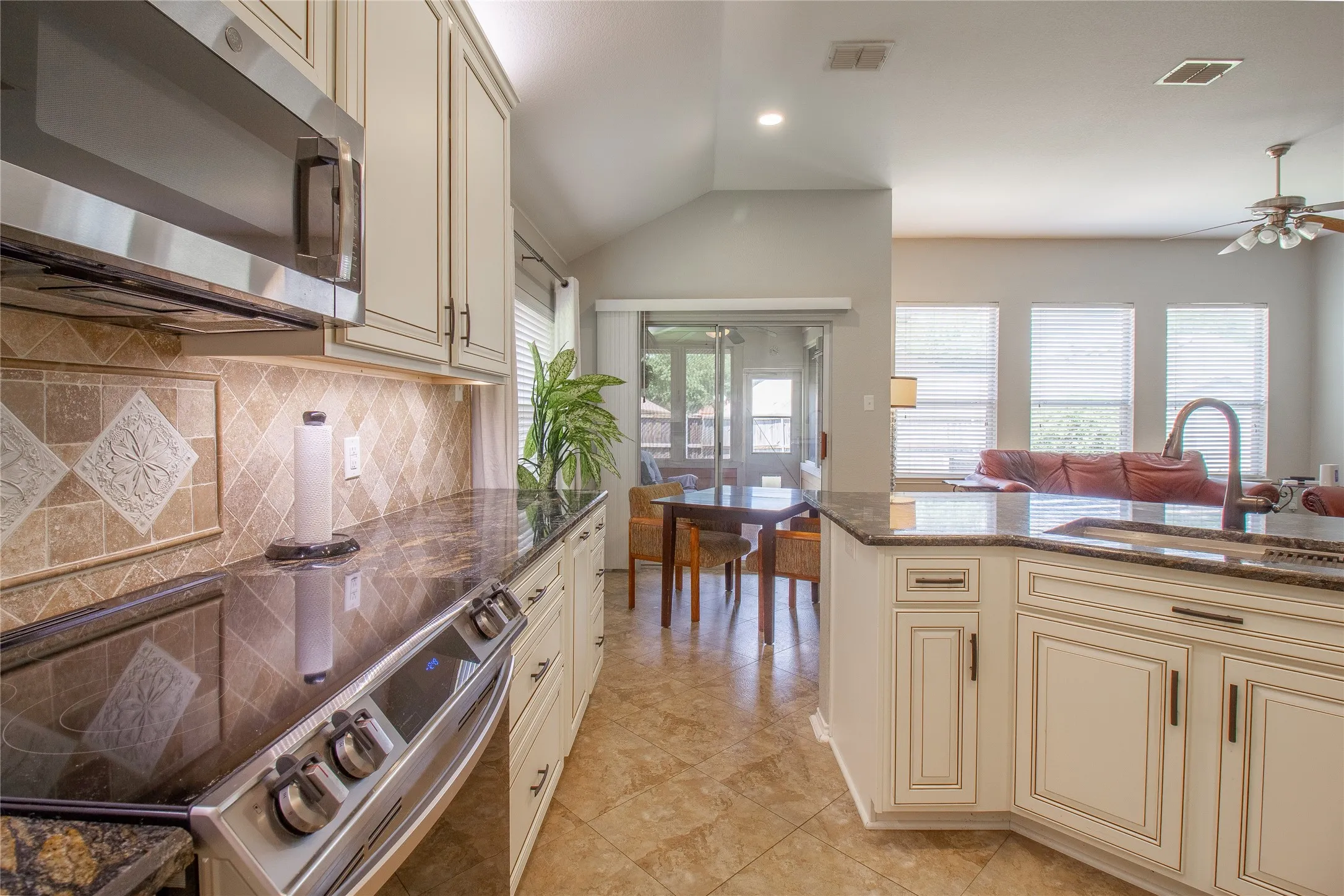 Kitchen featuring stainless steel appliances, granite countertops, tile backsplash, cream cabinetry, and tile flooring