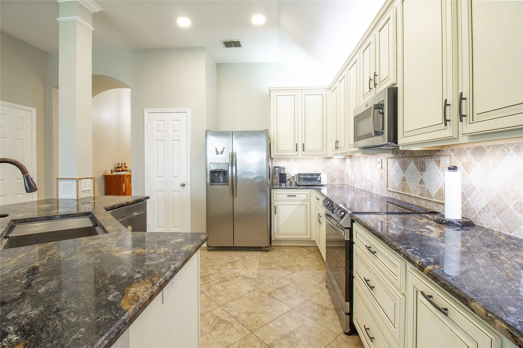 Kitchen featuring granite countertops, stainless steel appliances, light cabinetry, tile flooring, and recessed lighting