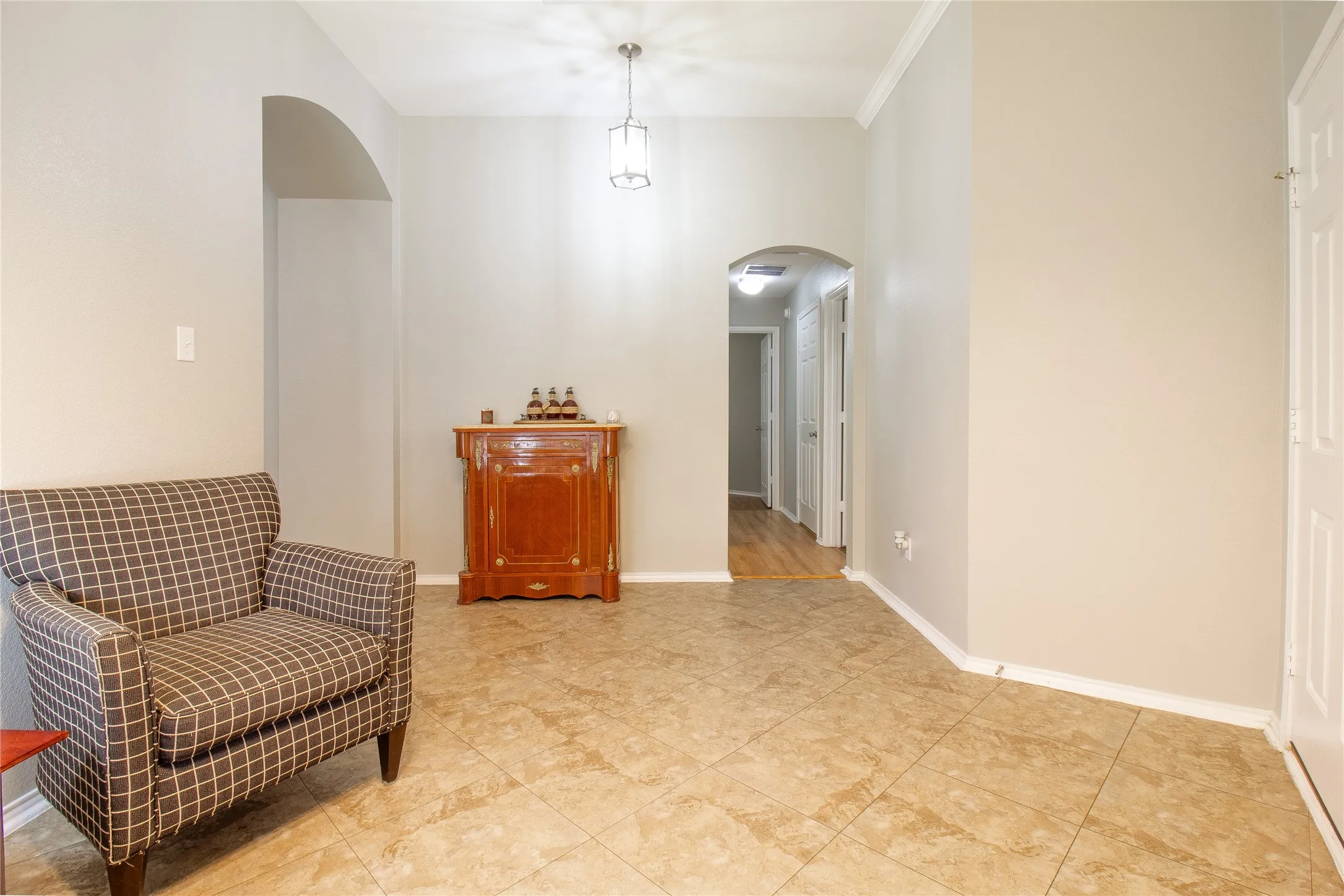 Warm neutral wall tones with crown molding, square tile flooring, and arched doorways
