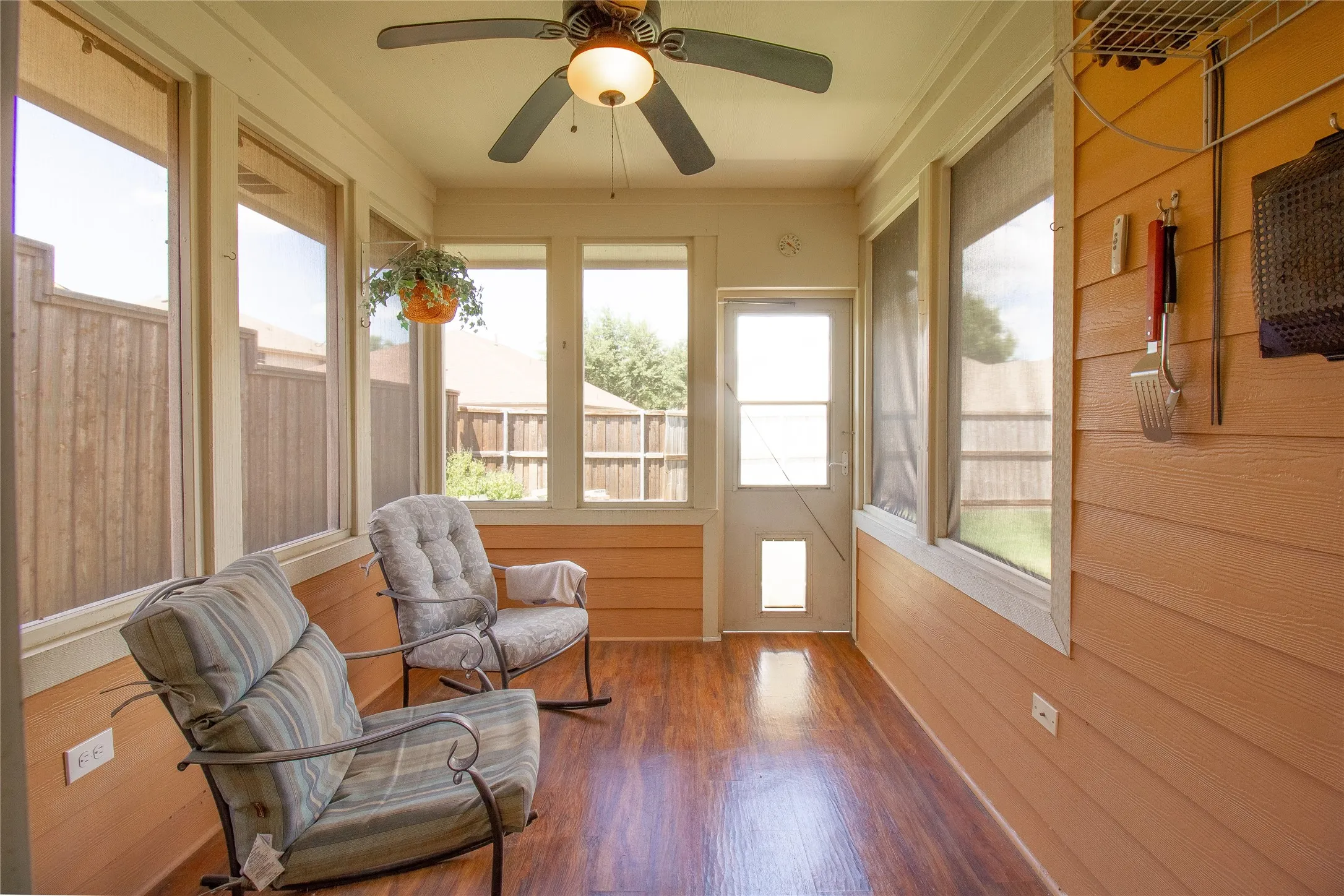 Enclosed patio featuring wood-finish flooring, a ceiling fan with integrated lighting, numerous windows, and a screen door with a pet access panel