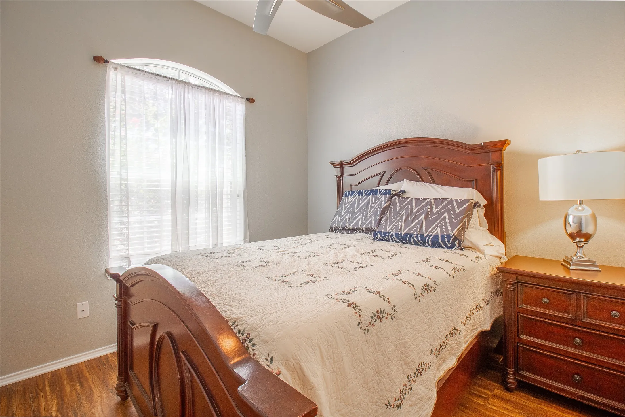 Bedroom featuring wood-finish flooring, a vaulted ceiling, and an arched window with blinds