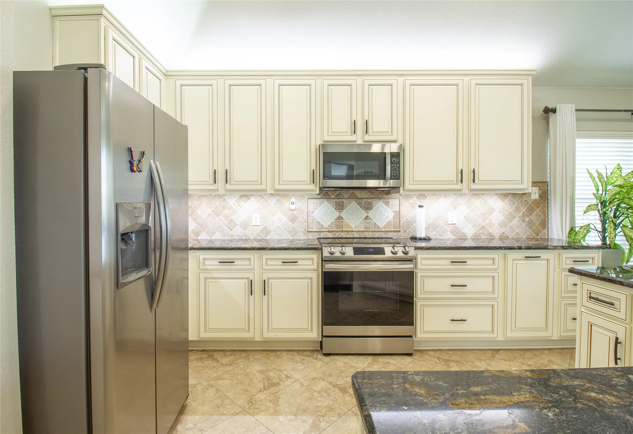Kitchen featuring cream-colored cabinetry, stainless steel appliances, dark stone countertops, and a patterned tile backsplash