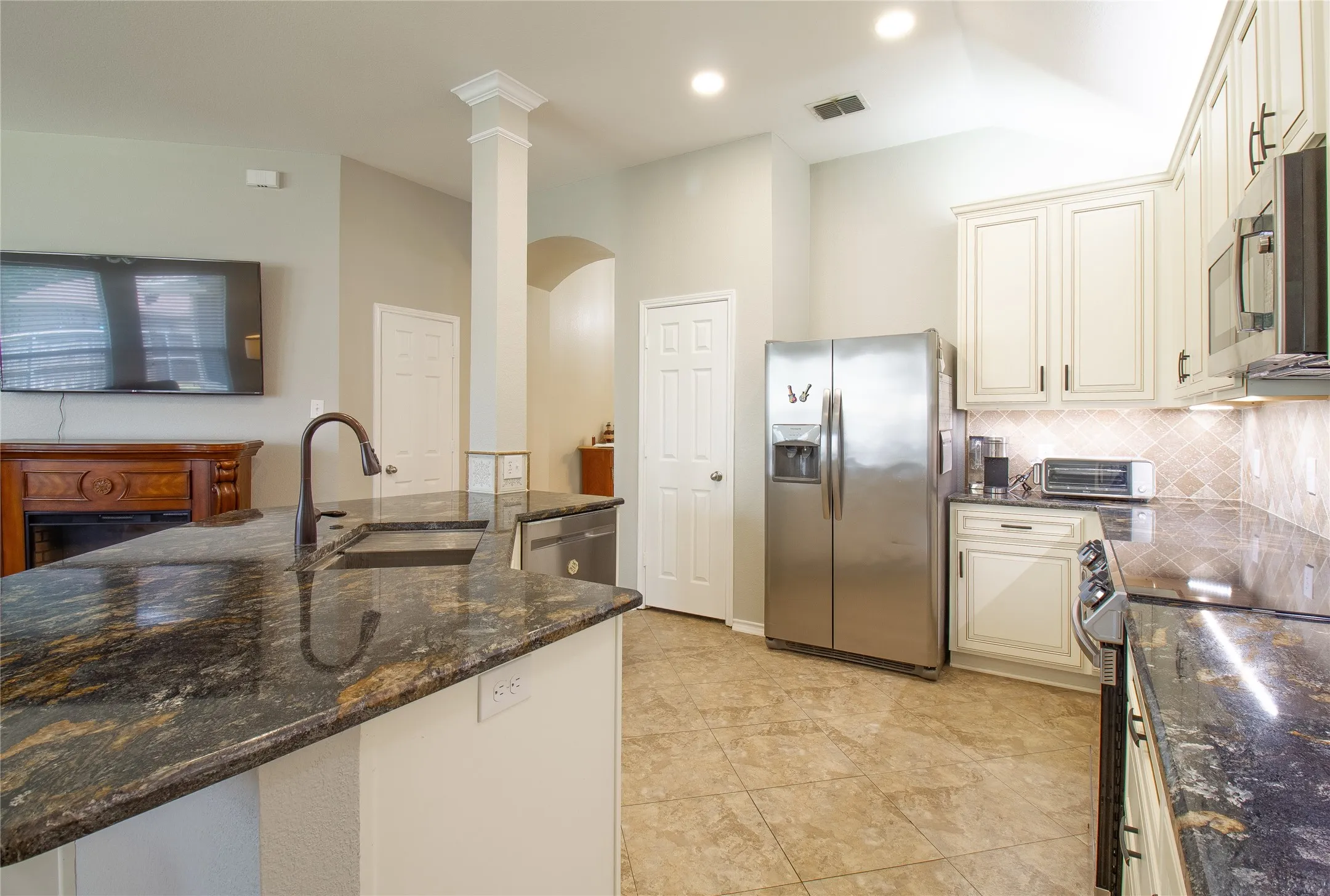 Kitchen featuring dark granite countertops, cream cabinetry with dark hardware, a stainless steel refrigerator, and tiled flooring