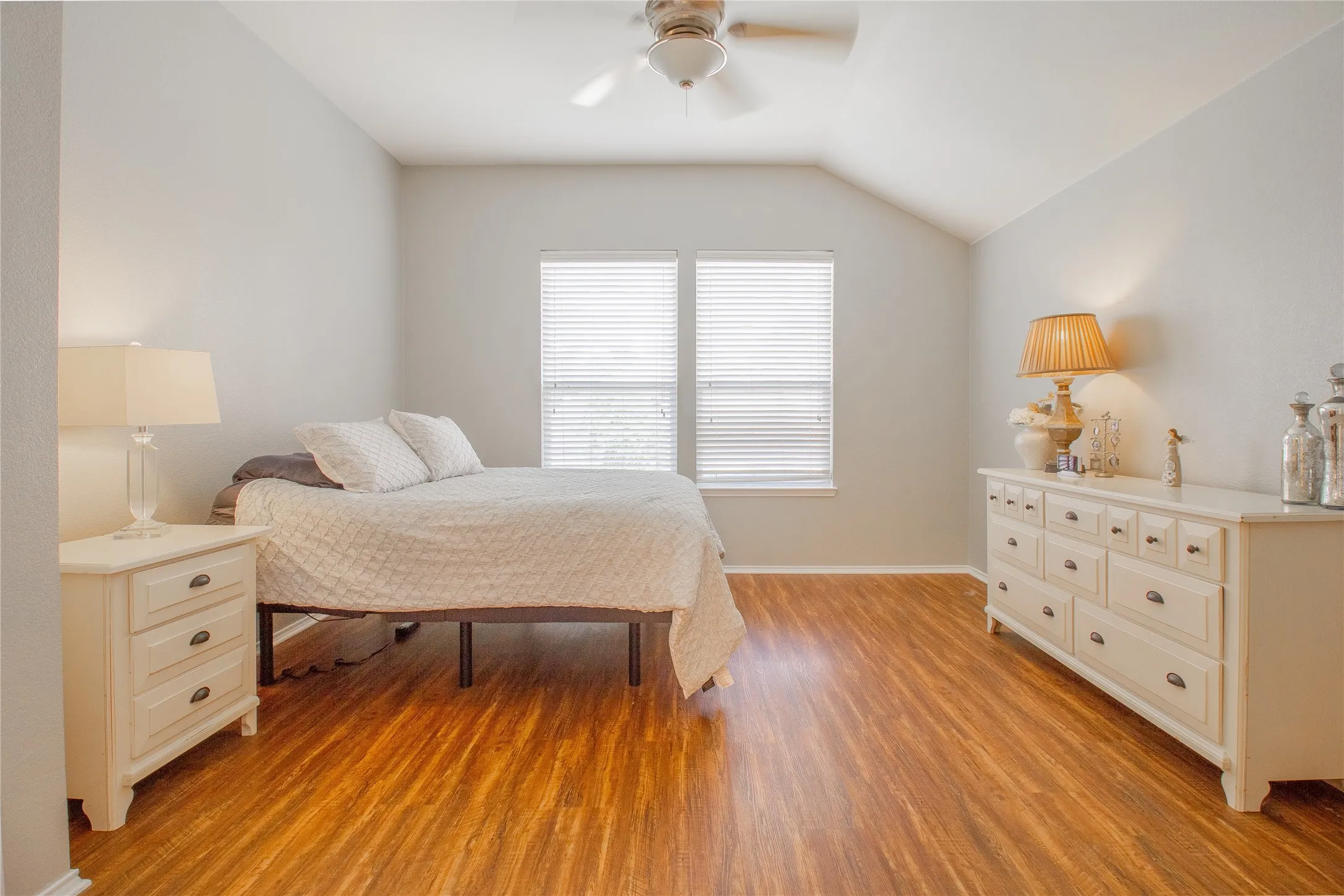 Spacious room featuring wood-finish flooring, vaulted ceilings, and a ceiling fan