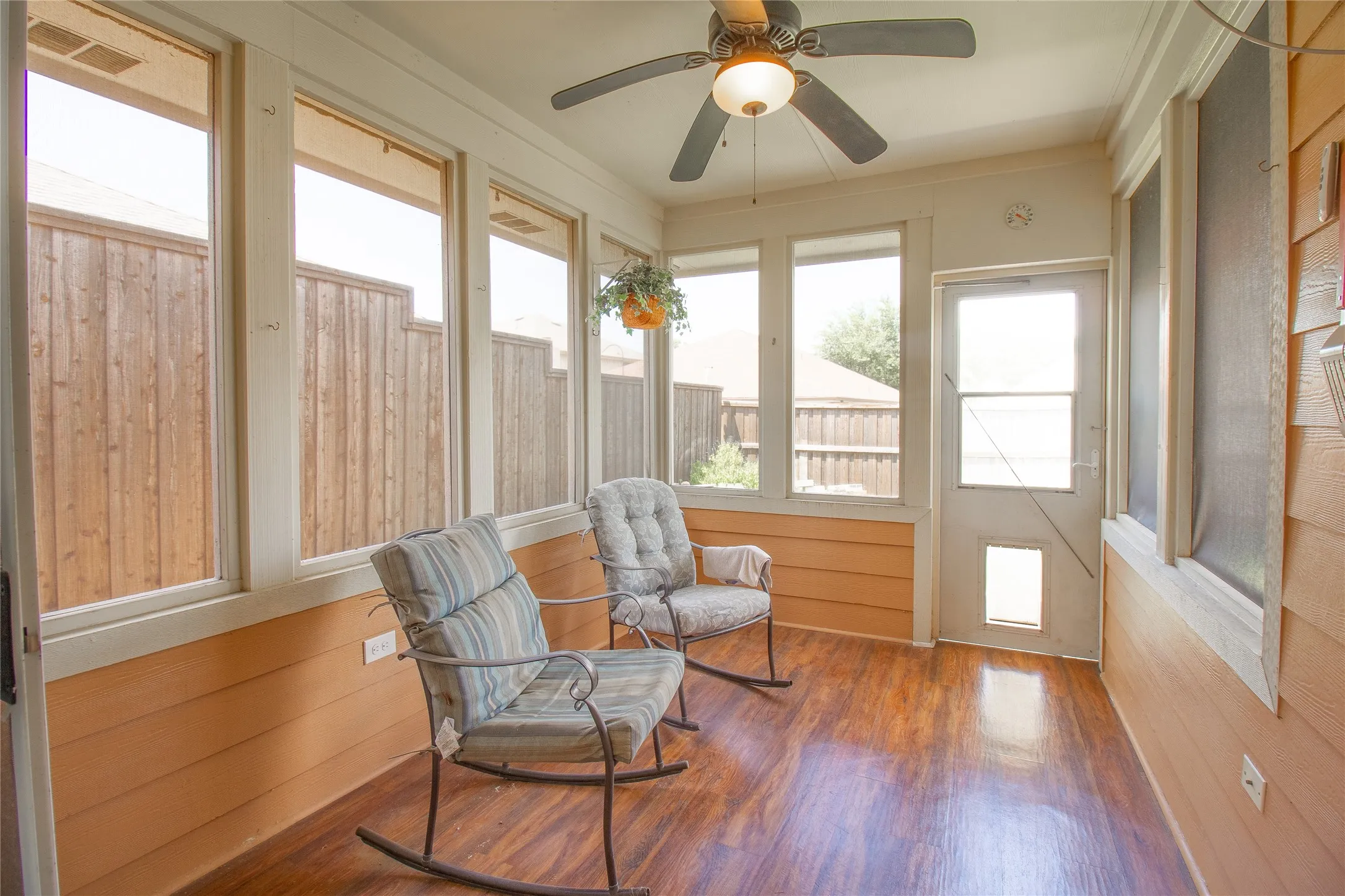 Enclosed sunroom featuring multiple large windows, wood-finish flooring, a ceiling fan with integrated lighting, and a rear door with a lower pet entrance