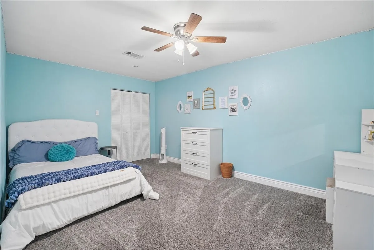 Bedroom featuring light blue walls, gray carpeting, a built-in closet with bi-fold doors, and a ceiling fan with light fixture