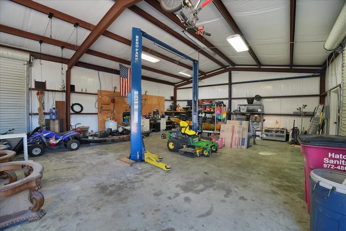 Spacious metal-framed workshop featuring a concrete floor, high vaulted ceiling, and multiple fluorescent light fixtures