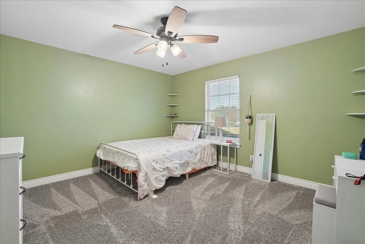 Bedroom featuring plush carpet, a ceiling fan with integrated lighting, window with blinds, and corner floating shelves