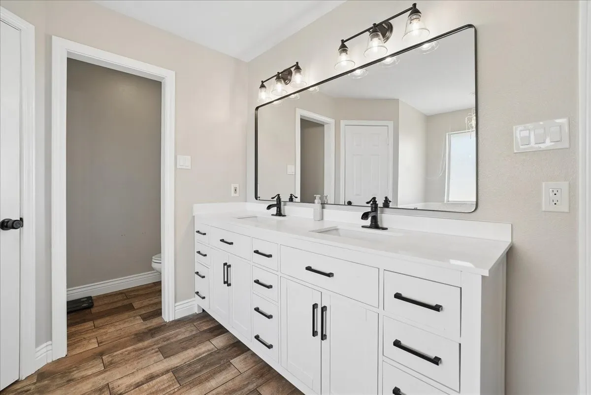 Dual sink vanity with white cabinetry, matte black hardware, and an expansive framed mirror