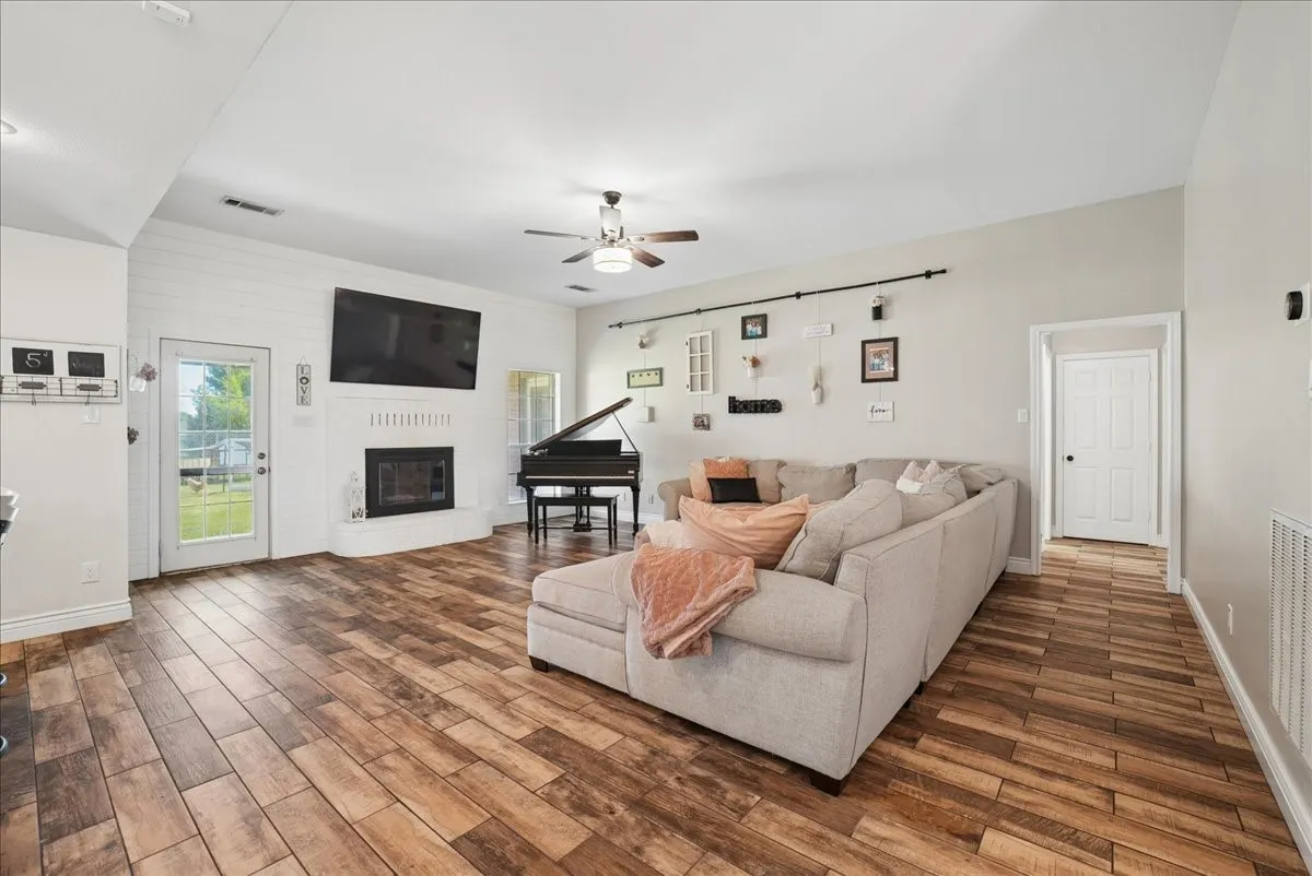 Spacious living area featuring wood-finish flooring, a white shiplap fireplace surround, and an exterior glass-paneled door