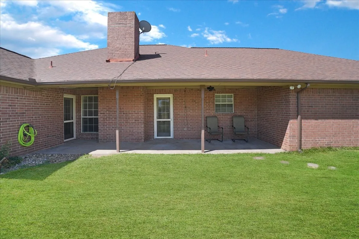 Brick exterior featuring a covered patio, multiple entry points, and an expansive lawn