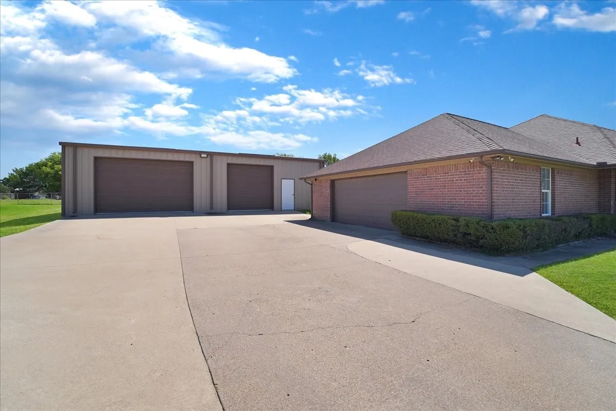 Expansive concrete driveway leading to a detached multi-bay metal building and an attached brick garage