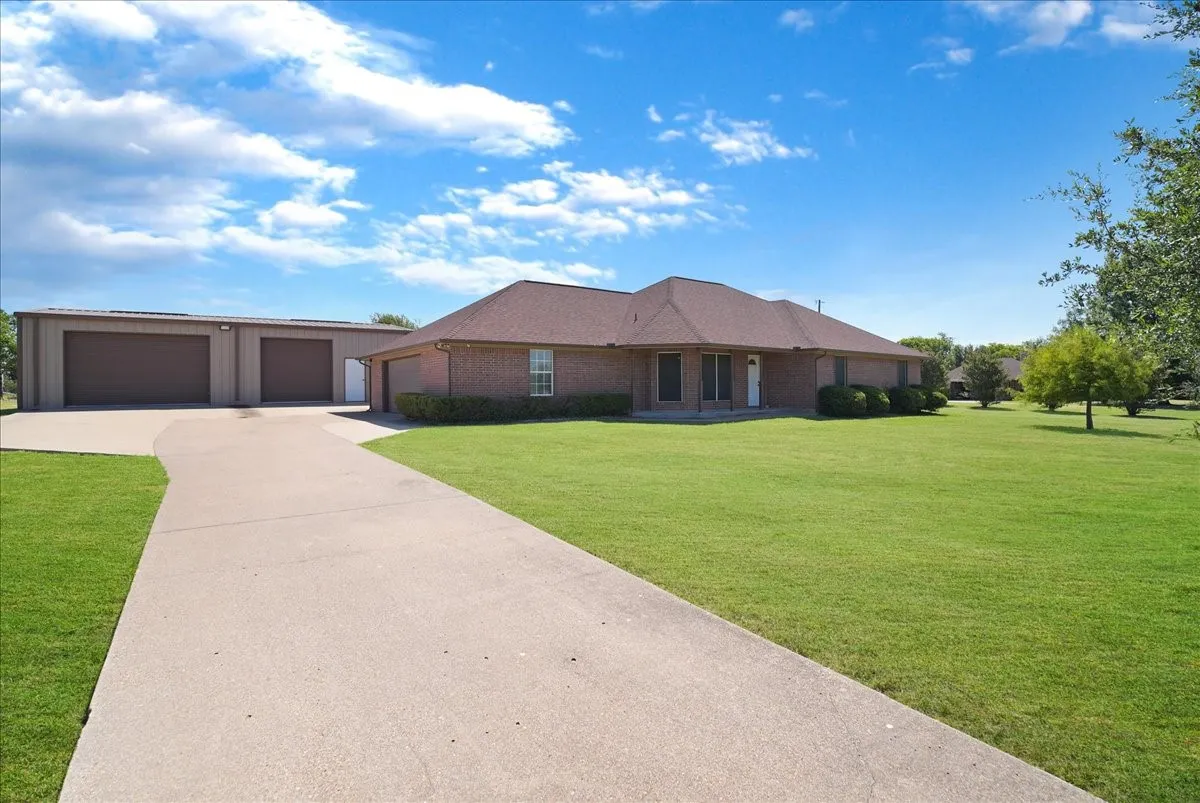 Brick exterior residence featuring a concrete driveway, two-car attached garage, and an additional detached three-bay garage structure