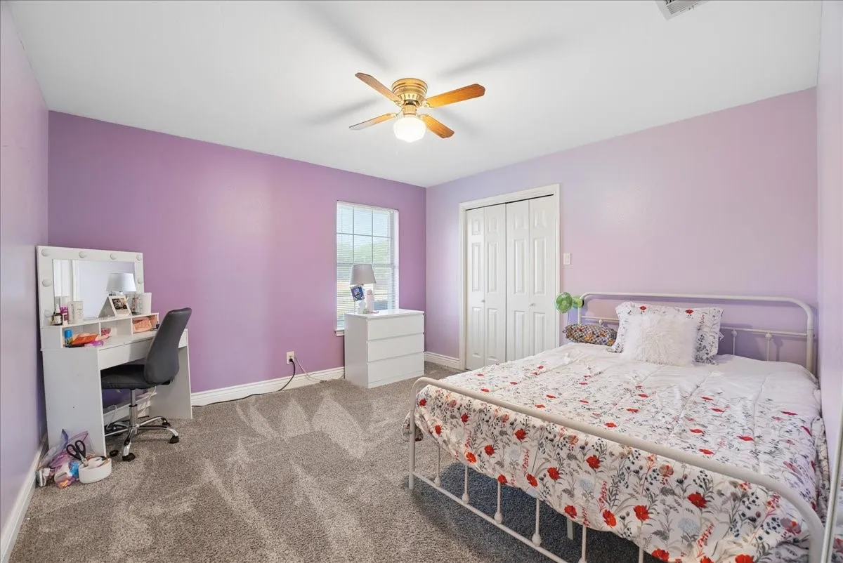 Carpeted interior room featuring a window, built-in closet with bi-fold doors, and a ceiling fan with light fixture