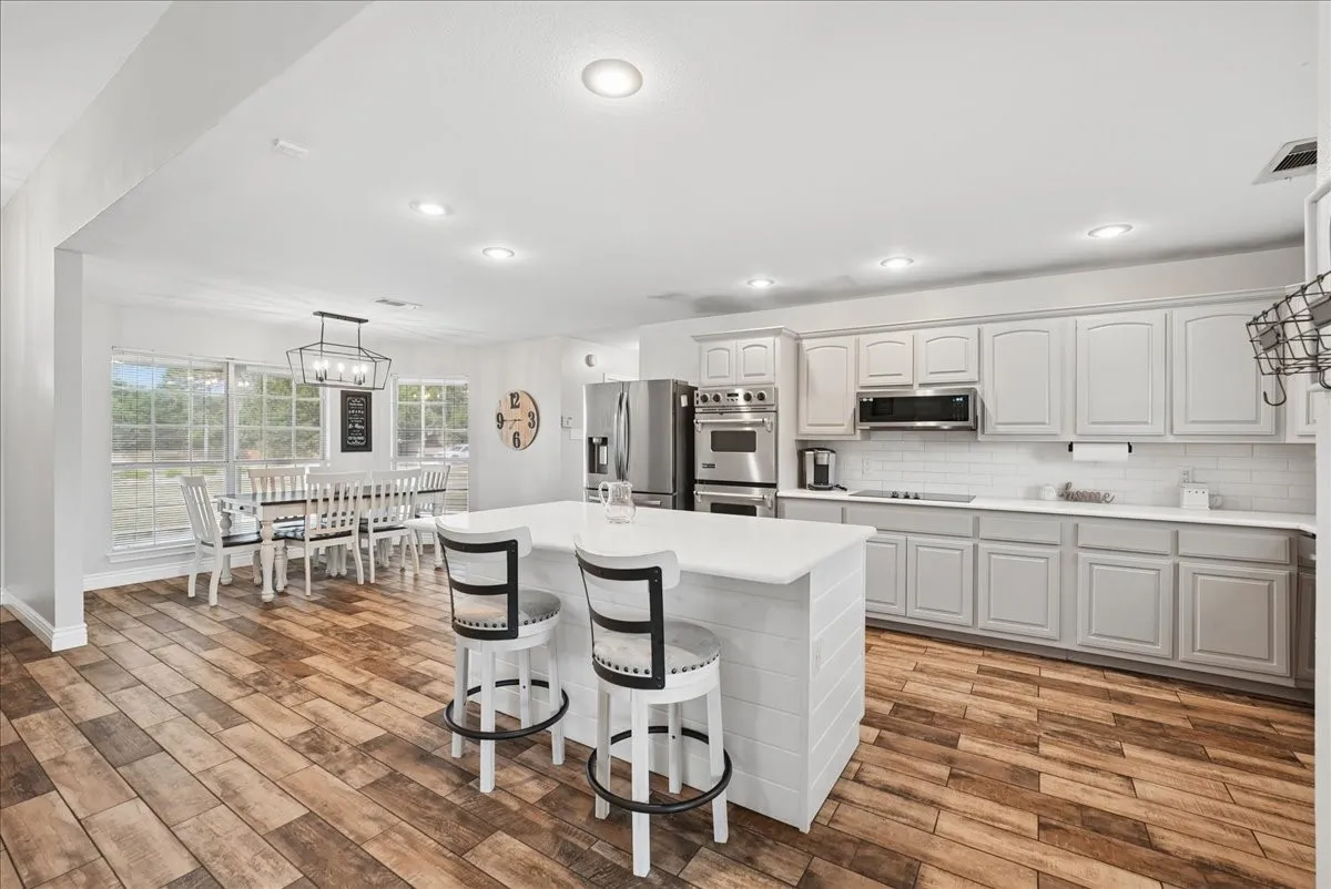 Modern kitchen featuring white shaker cabinetry, stainless steel appliances, a white subway tile backsplash, and wood-finish flooring