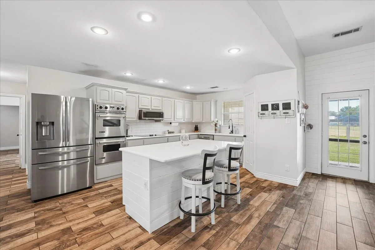 Bright kitchen featuring wood-finish flooring, white cabinetry, a central island with countertop seating, stainless steel appliances, and a glass-paned exterior door