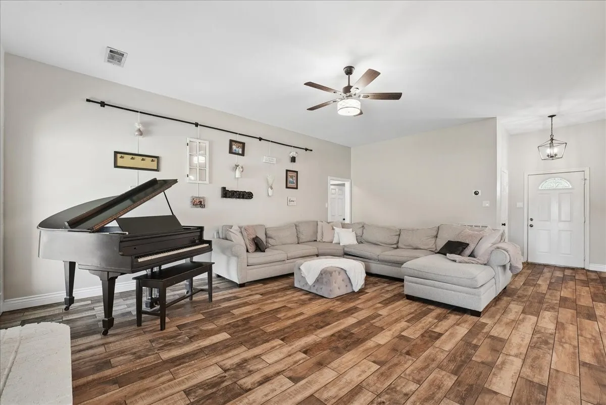 Spacious living area featuring wood-finish flooring, light-toned walls, and a ceiling fan