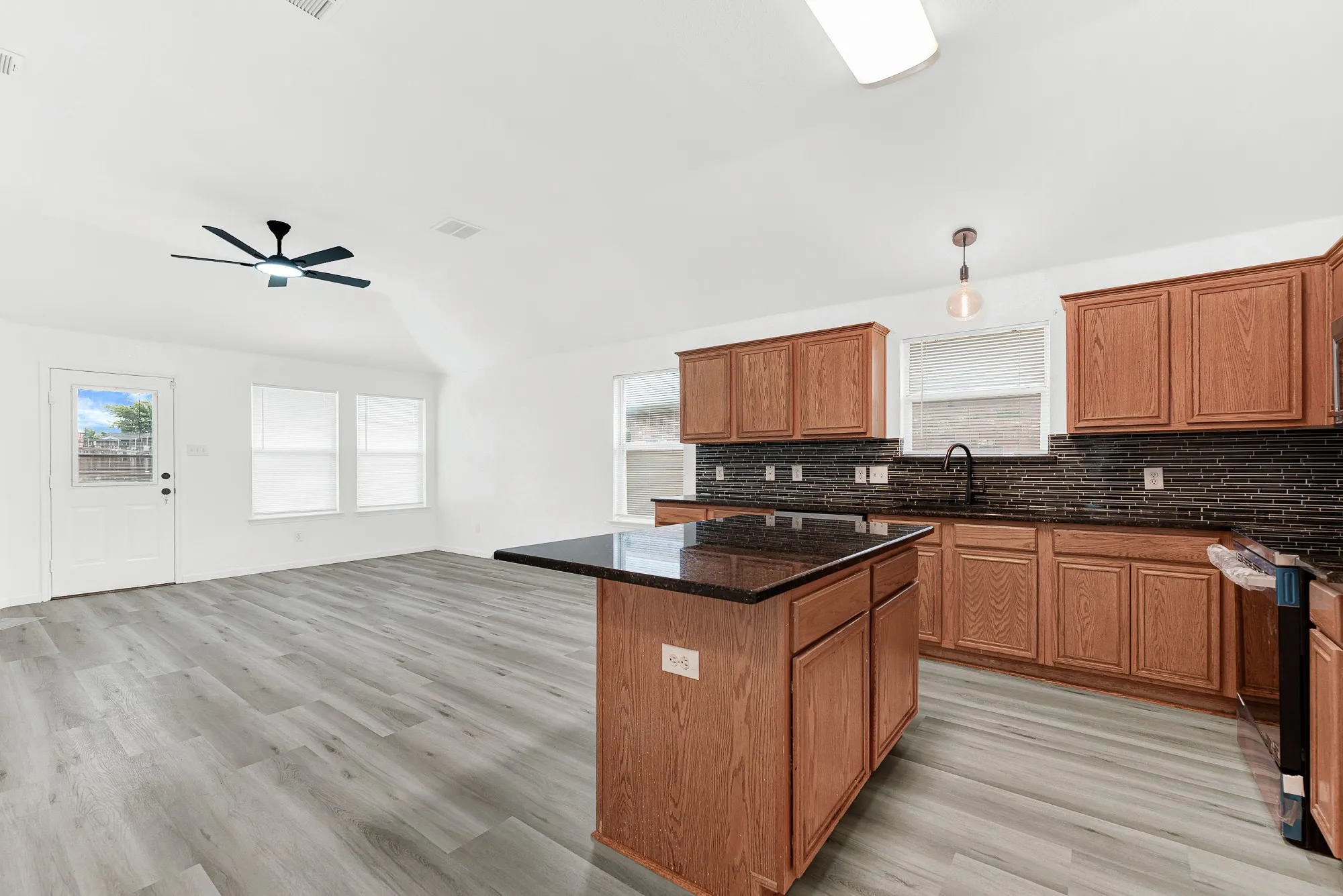 Kitchen featuring a central island with a dark countertop, wood-finish cabinetry, dark tile backsplash, and dark fixtures
