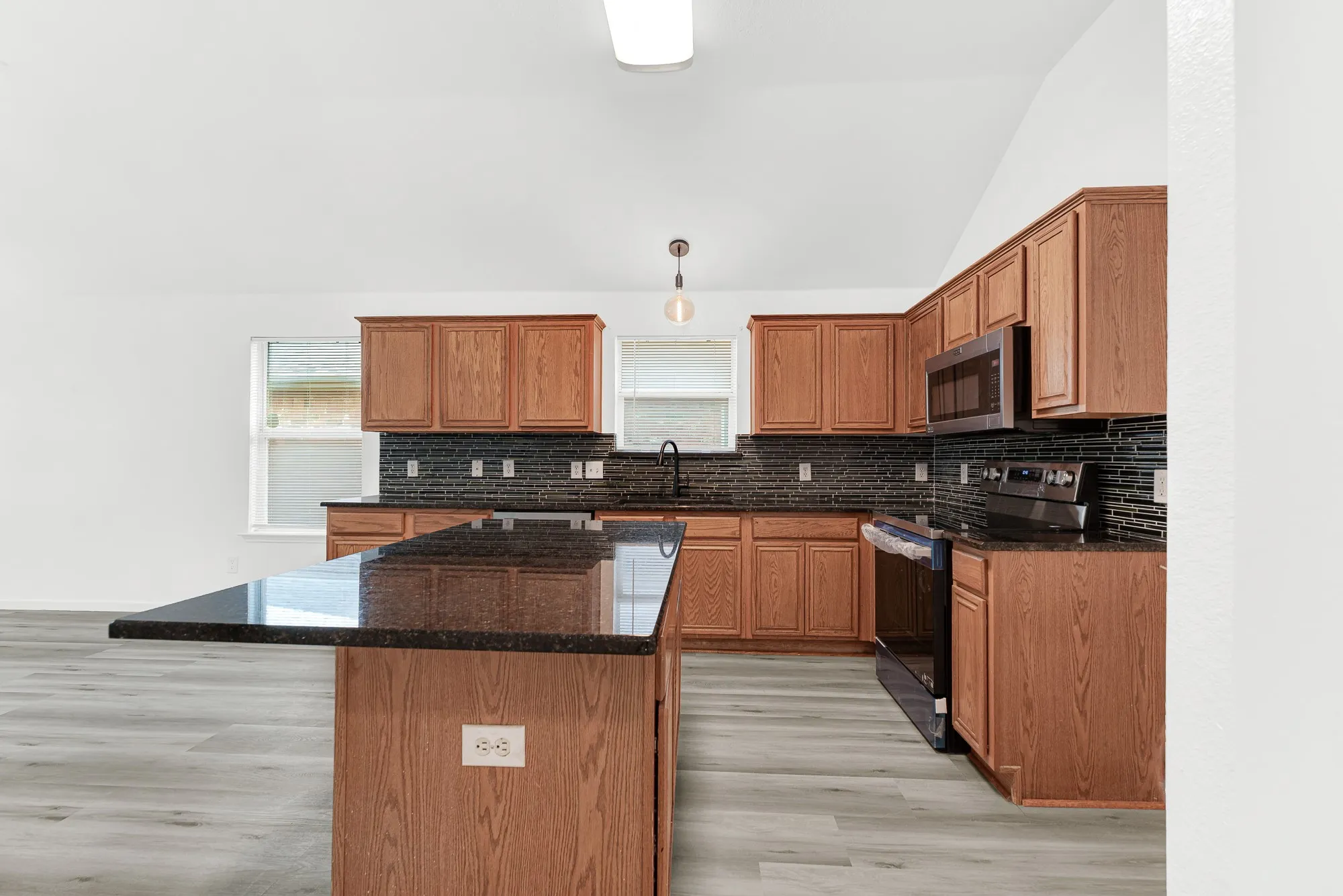 Kitchen featuring a large island with a dark countertop, extensive wood cabinetry, dark tile backsplash, and light wood-finish flooring