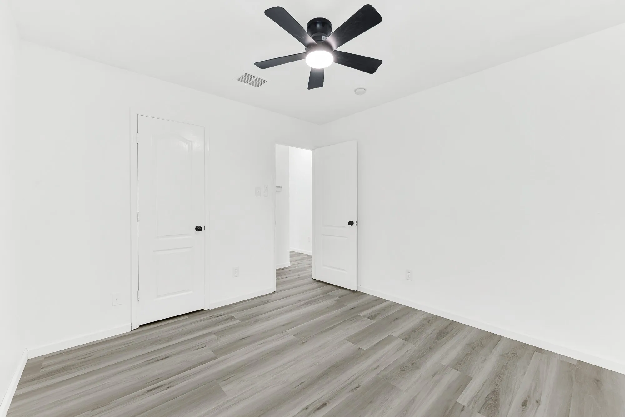 Room featuring wood-finish flooring, crisp white walls, and a contemporary black ceiling fan with integrated lighting