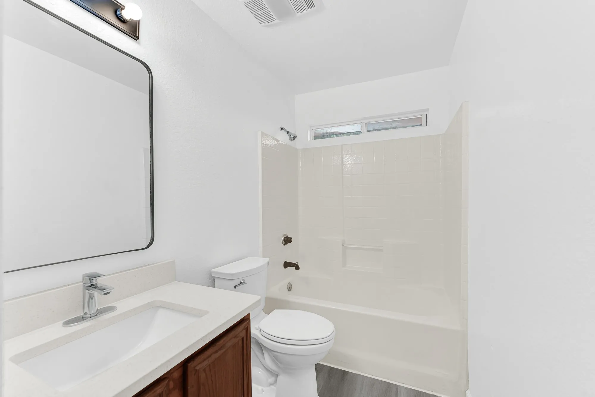 Bathroom featuring a wood-finish vanity with a light-toned countertop, an integrated rectangular sink, a contemporary chrome faucet, and a large wall-mounted mirror