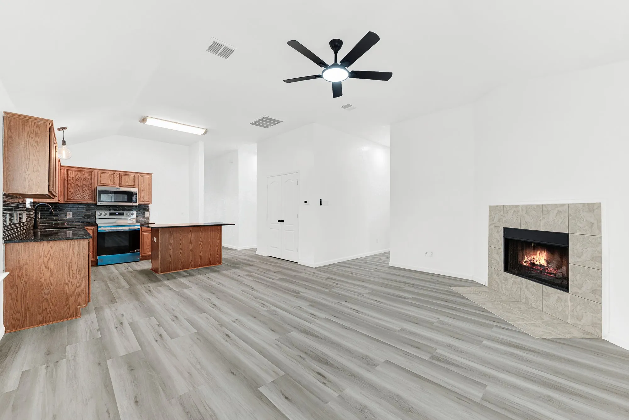 Spacious open-concept area featuring light wood-finish flooring, a contemporary ceiling fan, and a tiled fireplace