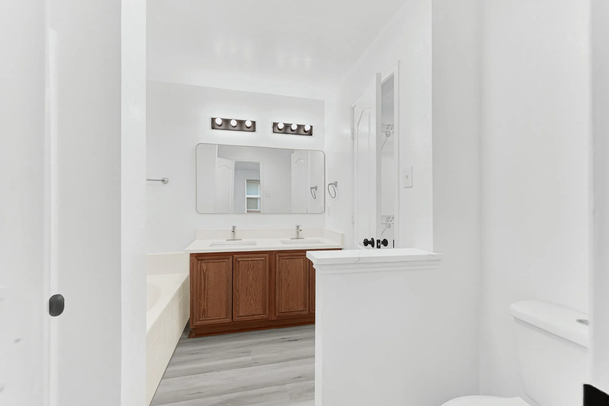 Bathroom featuring a dual vanity with a wood-finish cabinet and white countertop, undermount sinks, and wall-mounted light fixtures