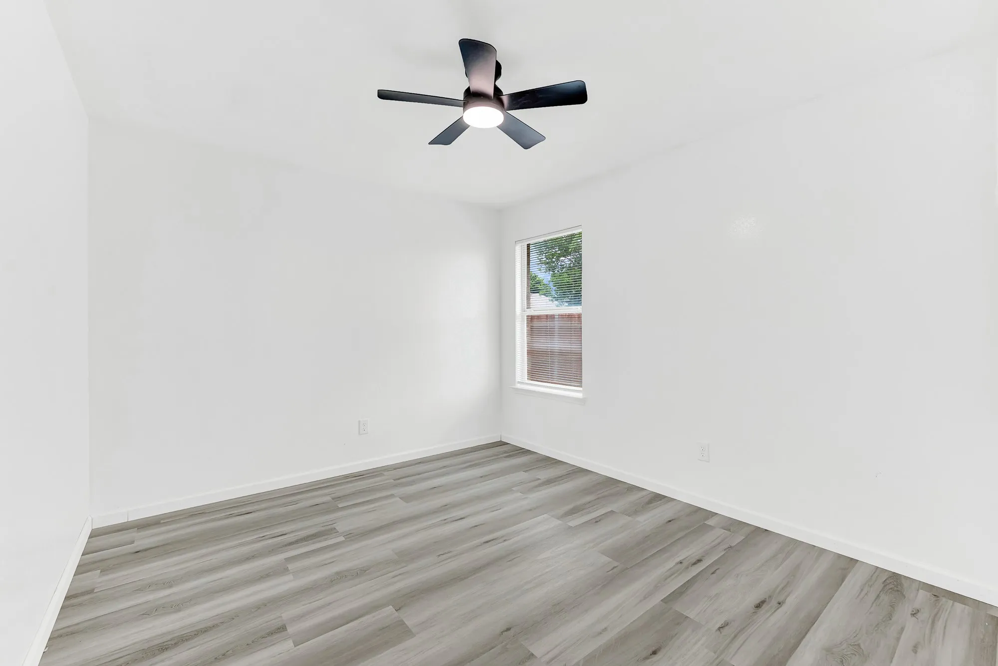 Room featuring light wood-finish flooring, white walls, and a window with white trim