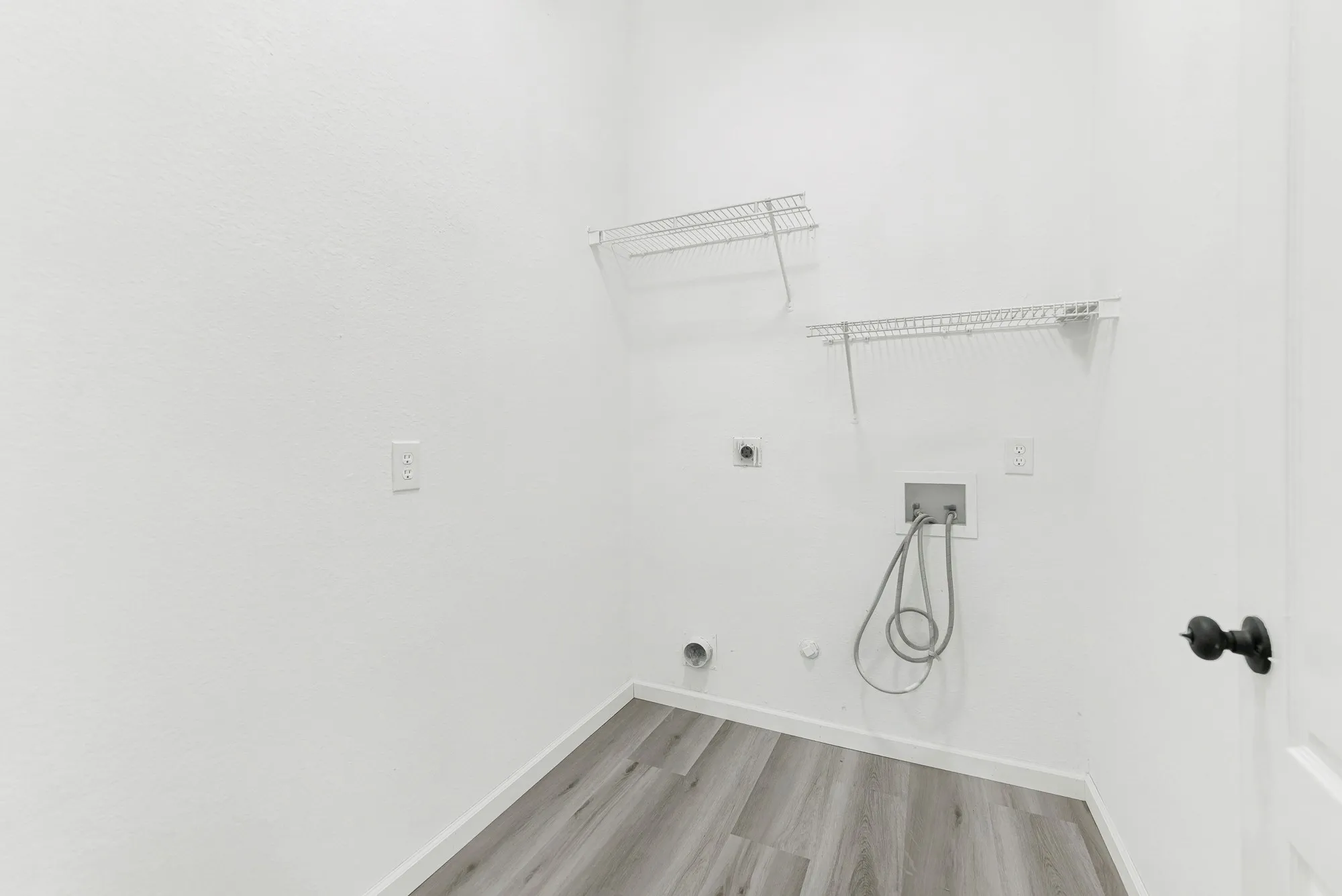 Dedicated utility space featuring wood-finish flooring, white walls, and pre-installed wire shelving