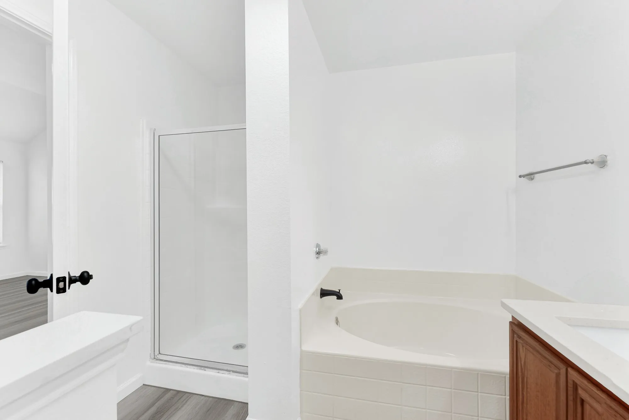Bathroom featuring a glass-enclosed shower, a built-in tub with tile surround, wood-finish flooring, and a vanity with a white countertop