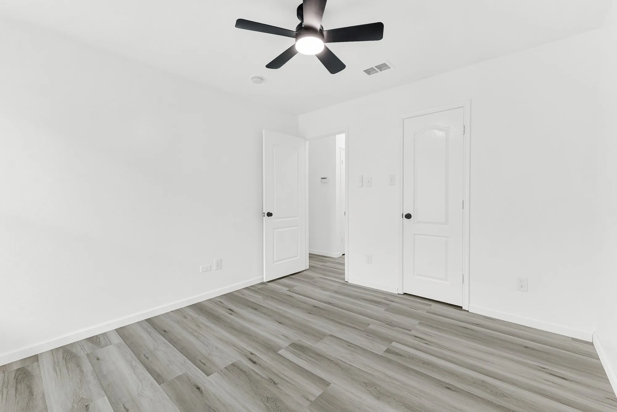 Bright room featuring wood-finish flooring, white walls, and a black ceiling fan with integrated lighting