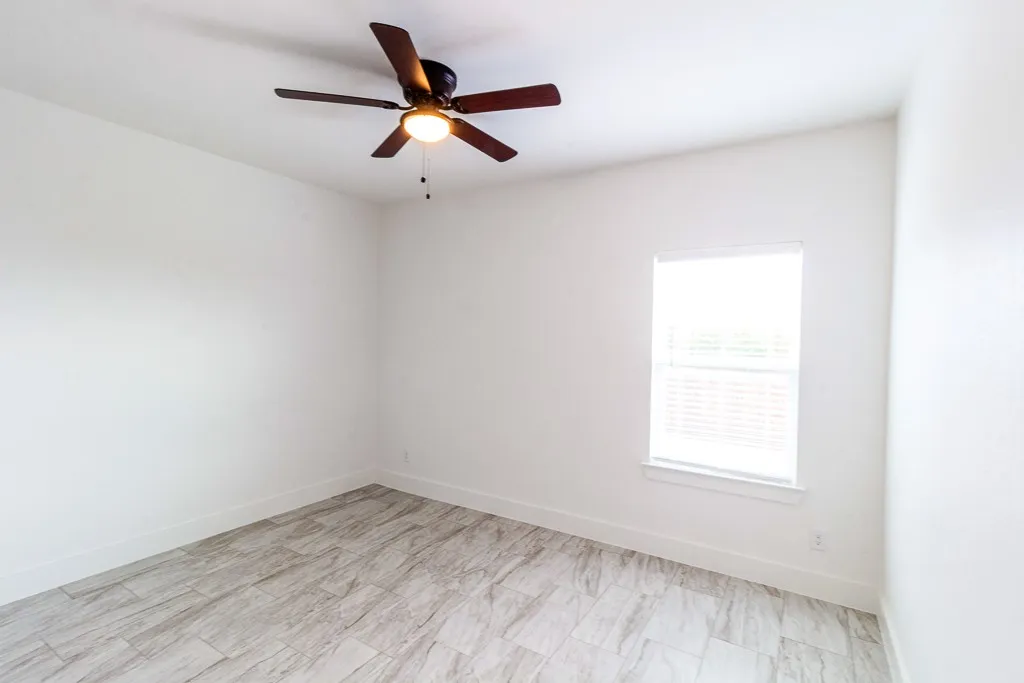 Bright bedroom showcasing wood-finish flooring, ceiling fan with integrated lighting, and large window providing natural light