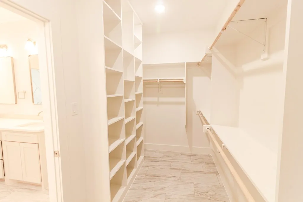 Spacious walk-in closet featuring custom built-in shelving and hanging rods throughout, wood-finish flooring, recessed lighting, and abundant storage capacity