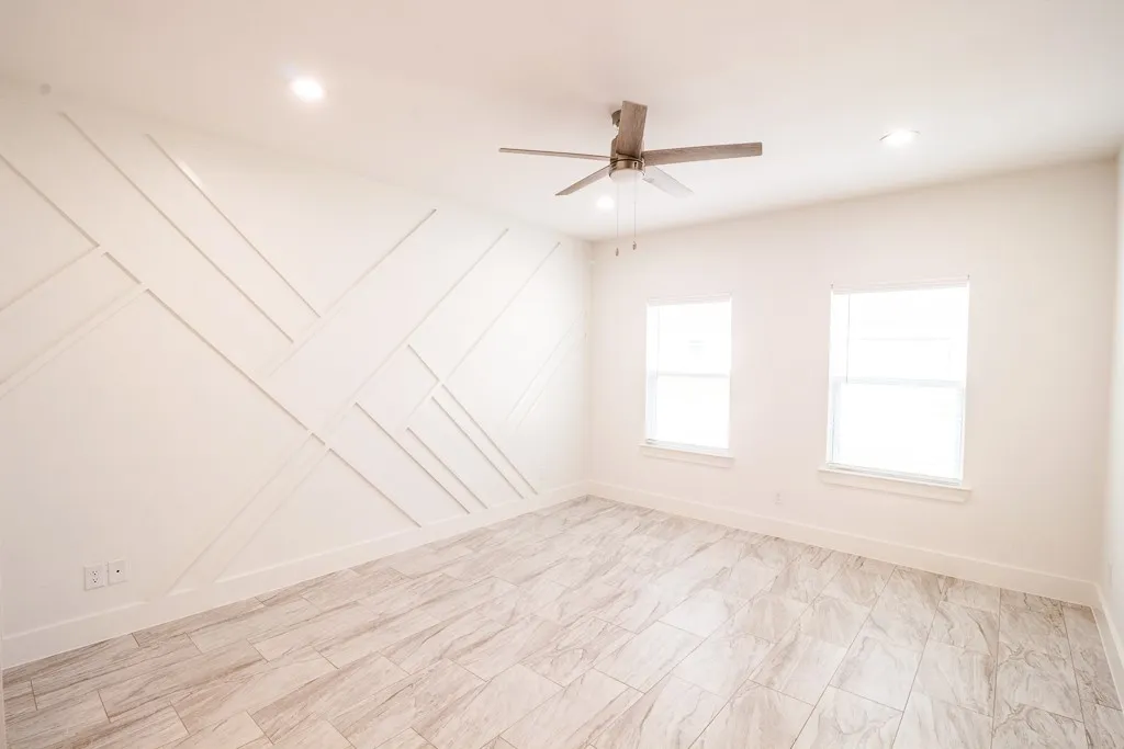 Bright and airy bedroom featuring recessed lighting, a modern ceiling fan with brushed metal finish, herringbone-pattern wood-finish flooring, and two large windows providing abundant natural light